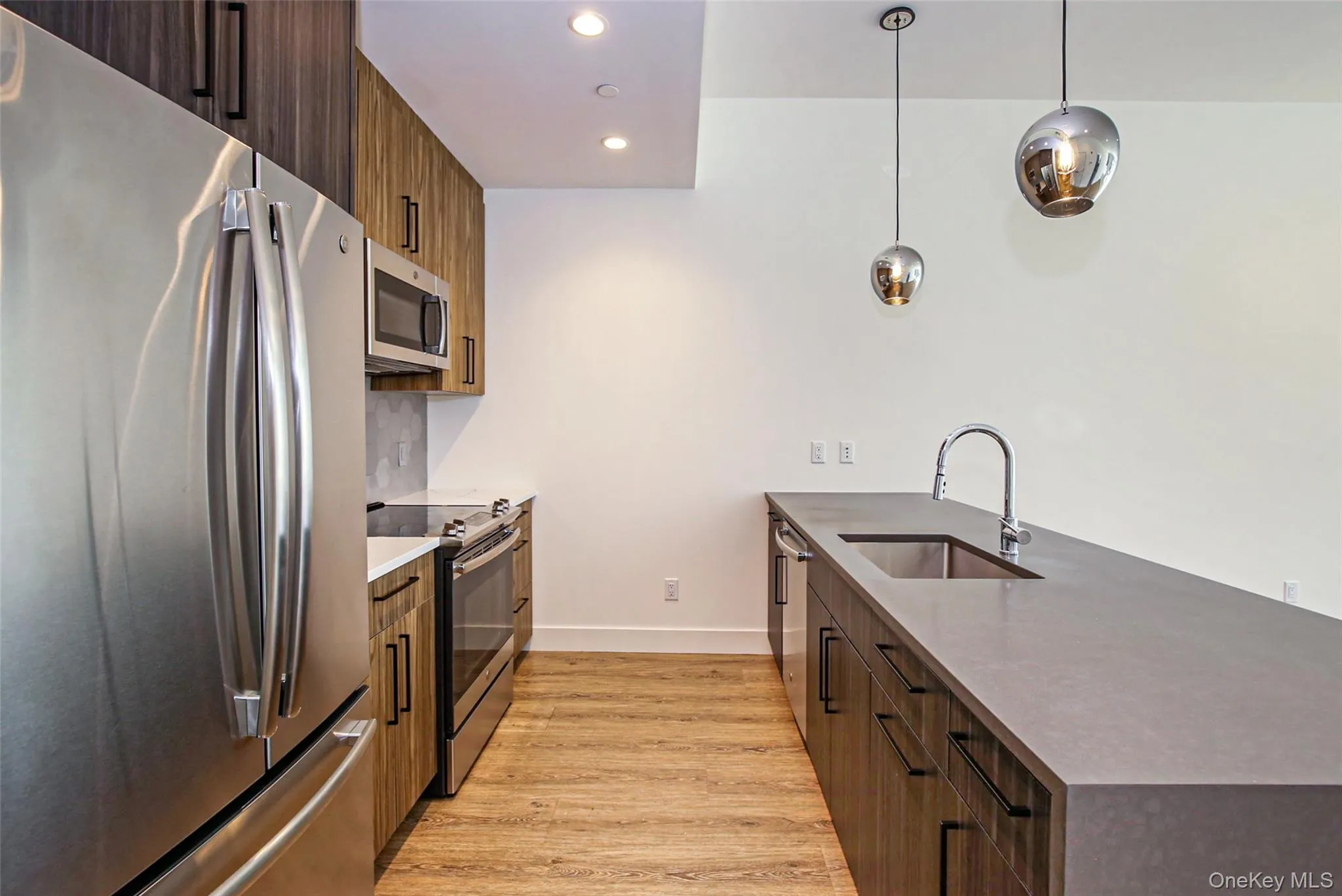 Kitchen with appliances with stainless steel finishes, a peninsula, light wood-type flooring, hanging light fixtures, and modern cabinets Kitchen with appliances with stainless steel finishes, a peninsula, light wood-type flooring, hanging light fixtures, and modern cabinets