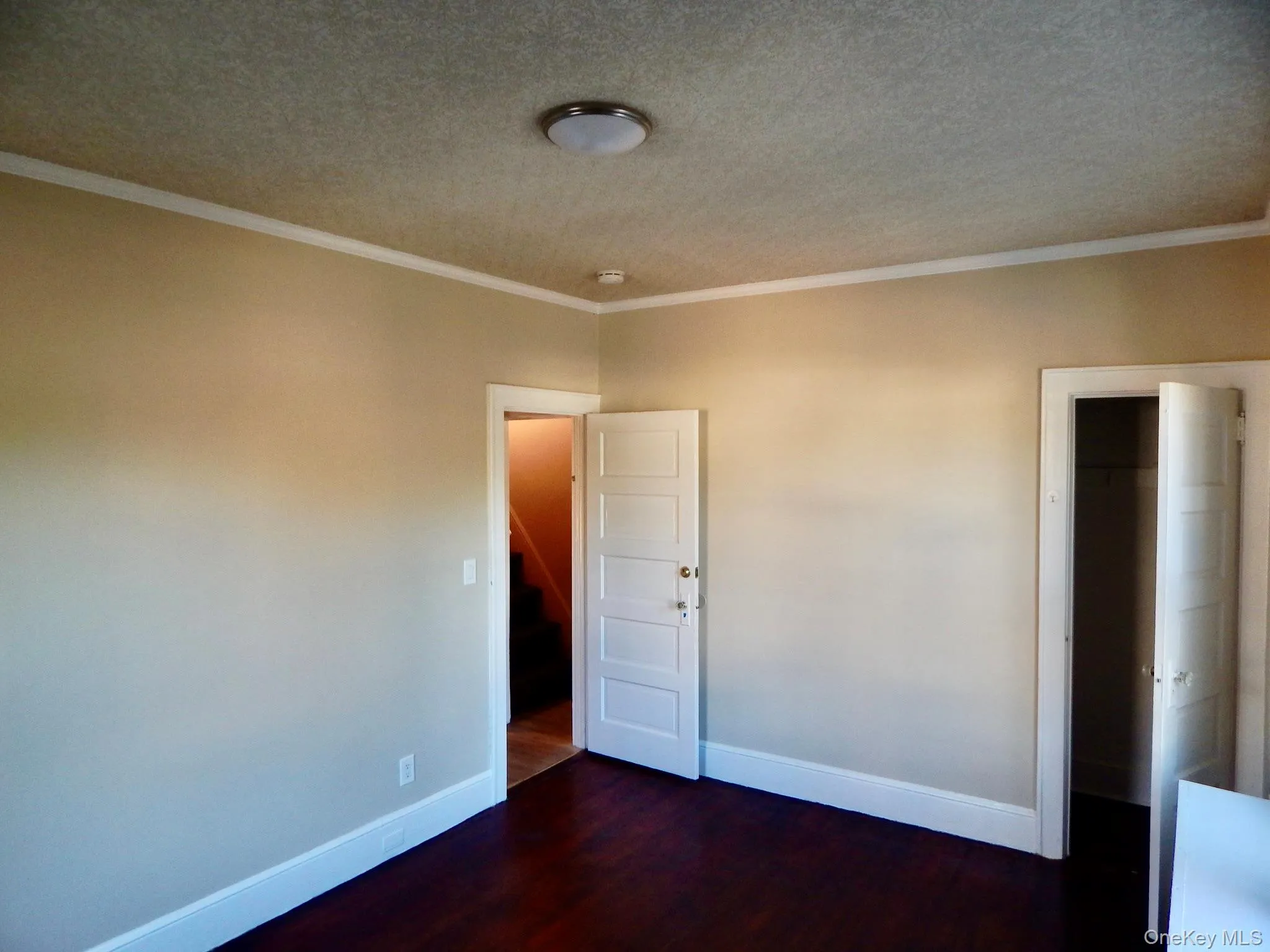 Unfurnished room with crown molding, dark wood-style flooring, a textured ceiling, and stairway Unfurnished room with crown molding, dark wood-style flooring, a textured ceiling, and stairway