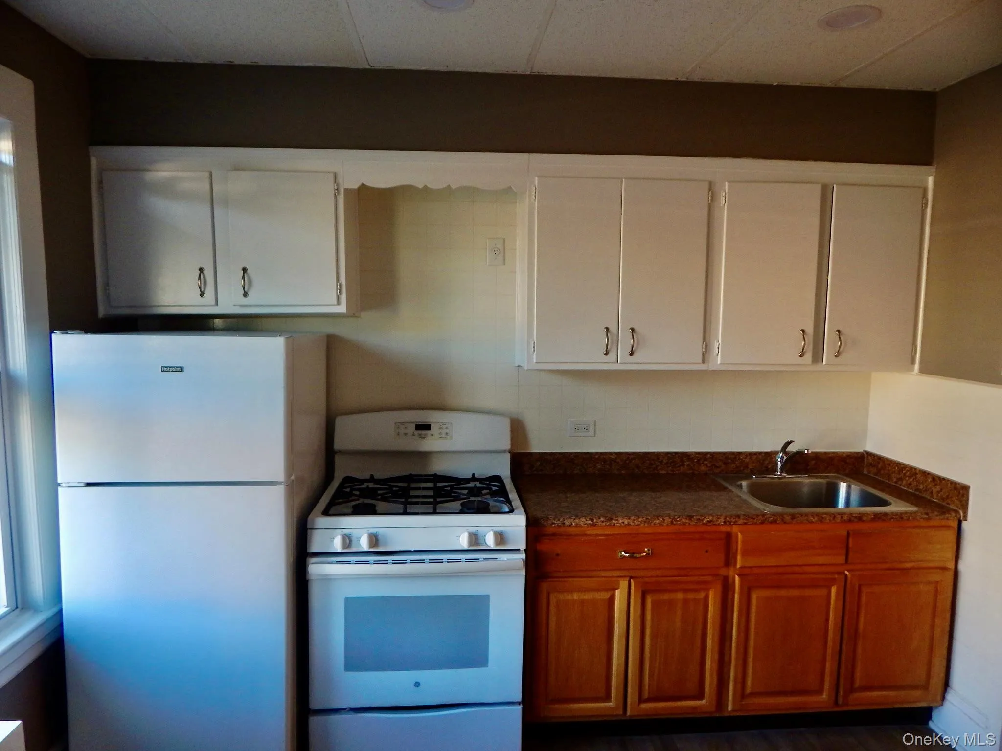 Kitchen with white appliances, dark wood-type flooring, a drop ceiling, and white cabinetry Kitchen with white appliances, dark wood-type flooring, a drop ceiling, and white cabinetry