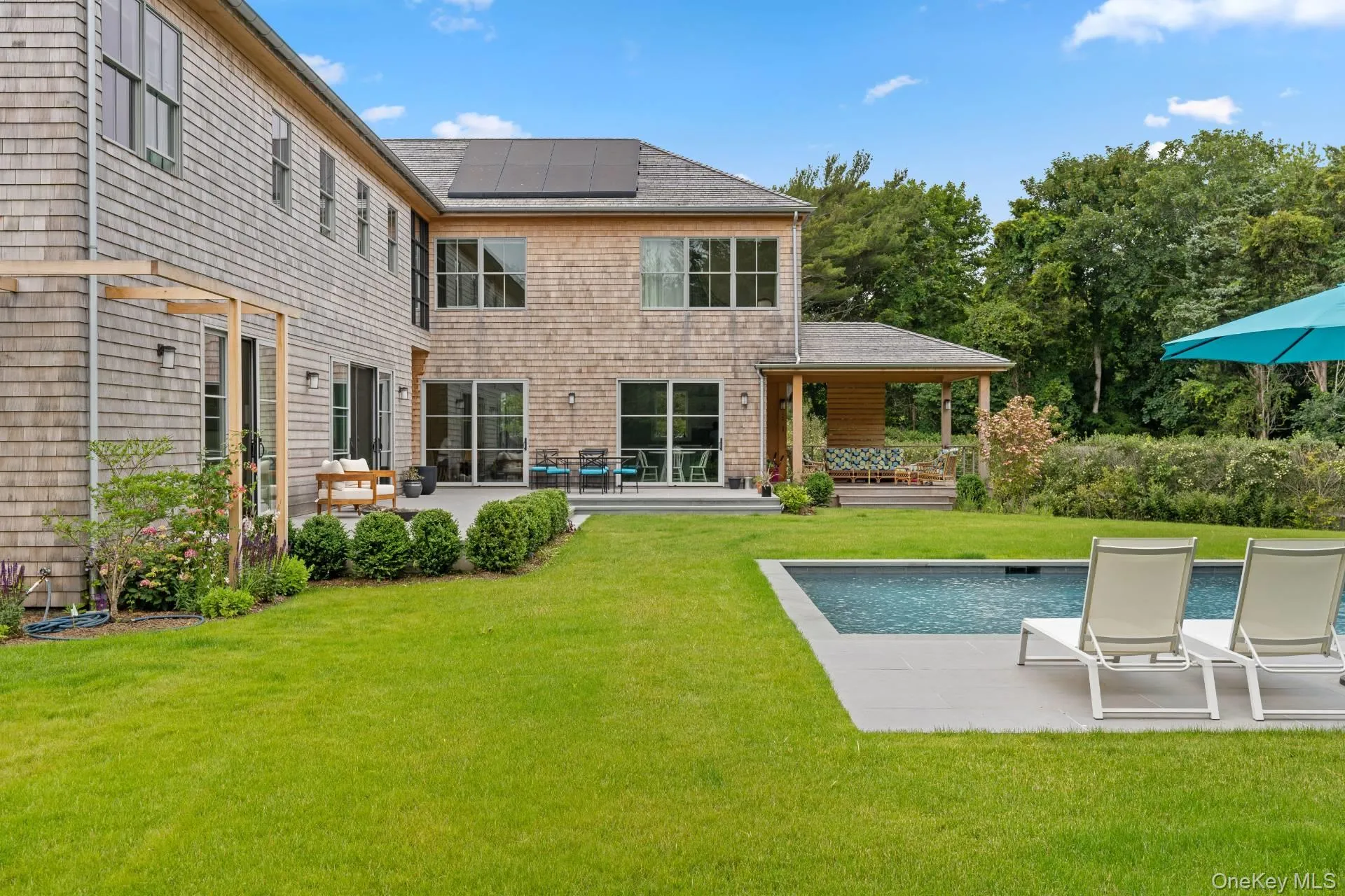 Rear view of property featuring solar panels, a patio area, a lawn, and roof with shingles Rear view of property featuring solar panels, a patio area, a lawn, and roof with shingles
