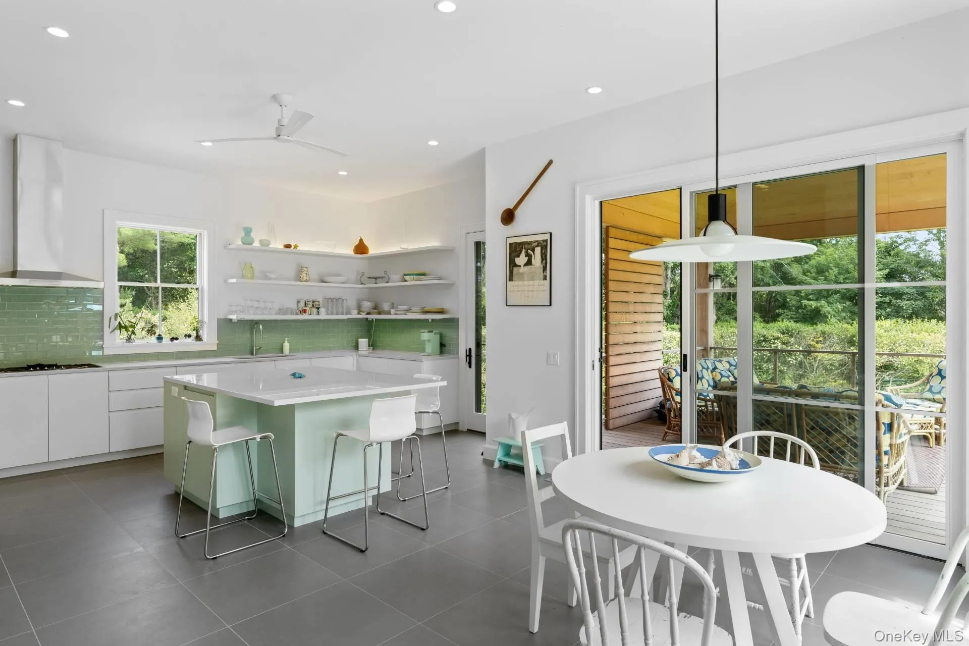 Kitchen with white cabinetry, wall chimney range hood, a kitchen bar, open shelves, and a kitchen island Kitchen with white cabinetry, wall chimney range hood, a kitchen bar, open shelves, and a kitchen island