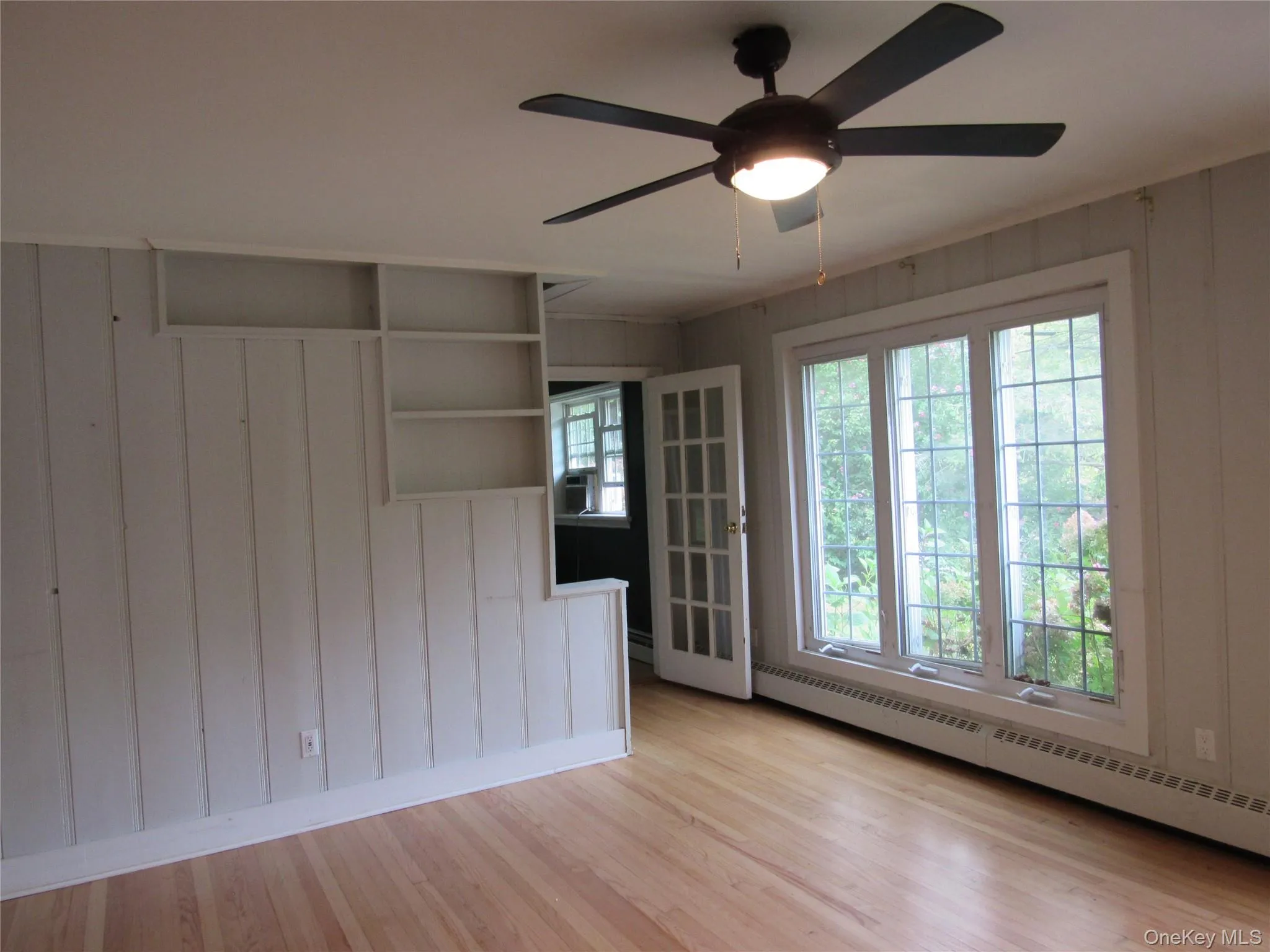Living room with light wood-style floors, ceiling fan, a baseboard radiator, plenty of natural light, and wooden walls Living room with light wood-style floors, ceiling fan, a baseboard radiator, plenty of natural light, and wooden walls