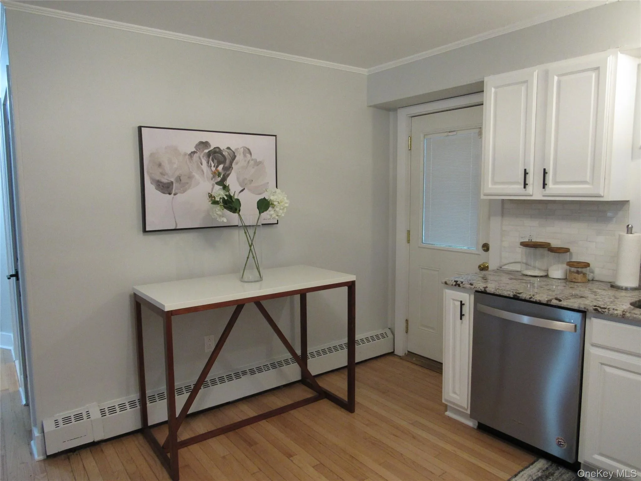 Kitchen featuring white cabinets, baseboard heating, light stone counters, dishwasher, and ornamental molding Kitchen featuring white cabinets, baseboard heating, light stone counters, dishwasher, and ornamental molding