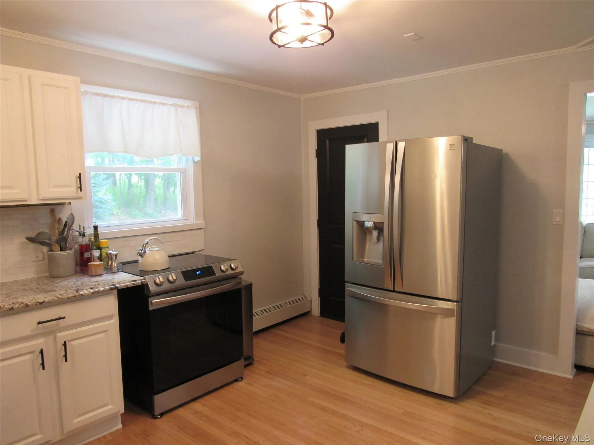 Kitchen with stainless steel appliances, light wood finished floors, white cabinetry, light stone counters, and crown molding Kitchen with stainless steel appliances, light wood finished floors, white cabinetry, light stone counters, and crown molding