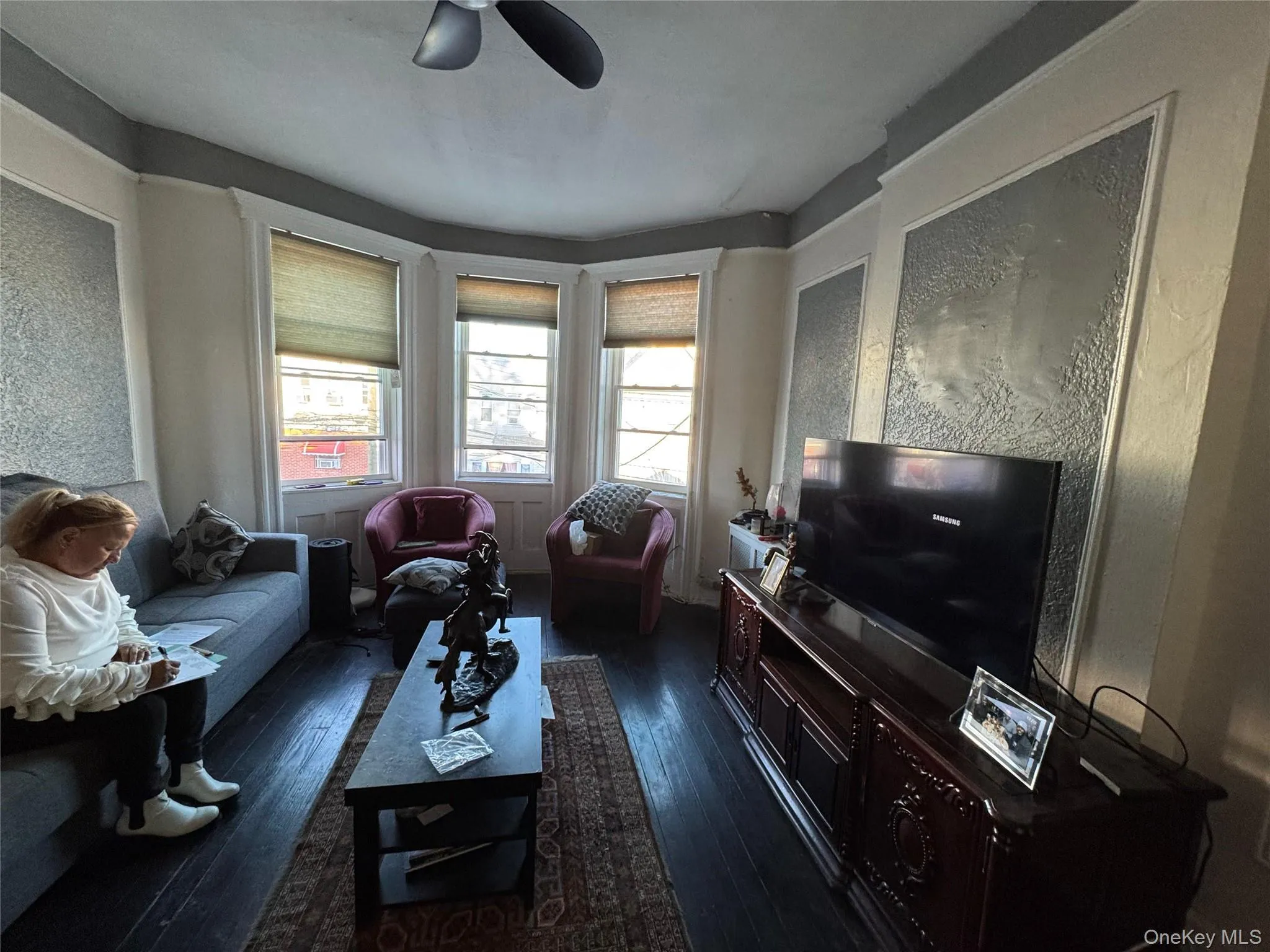 Living area with dark wood-type flooring, a textured wall, and a ceiling fan Living area with dark wood-type flooring, a textured wall, and a ceiling fan