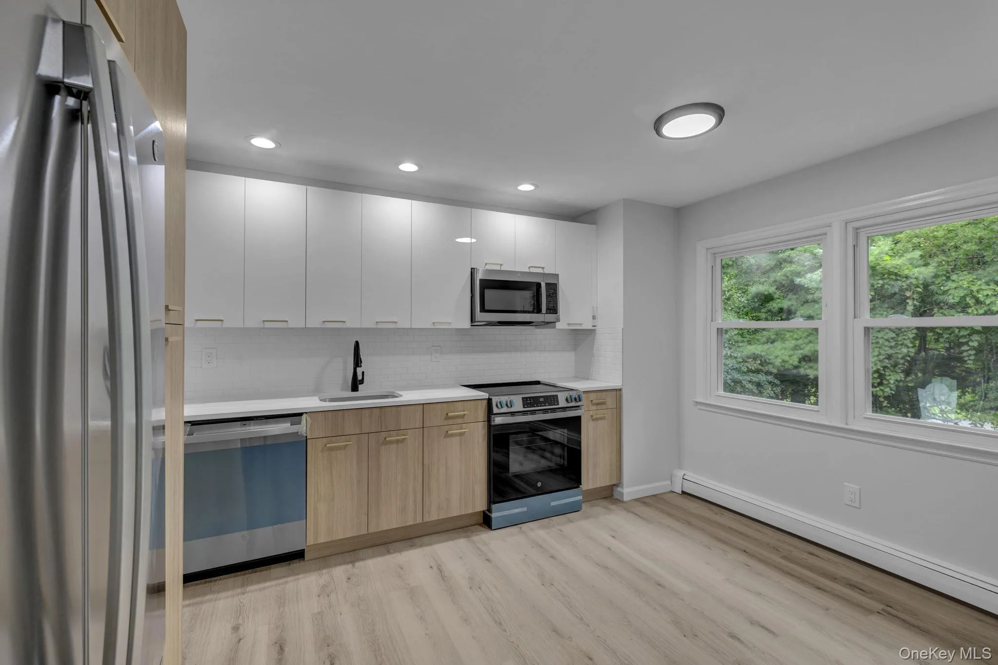 Kitchen featuring stainless steel appliances, modern cabinets, backsplash, baseboard heating, and white cabinetry Kitchen featuring stainless steel appliances, modern cabinets, backsplash, baseboard heating, and white cabinetry