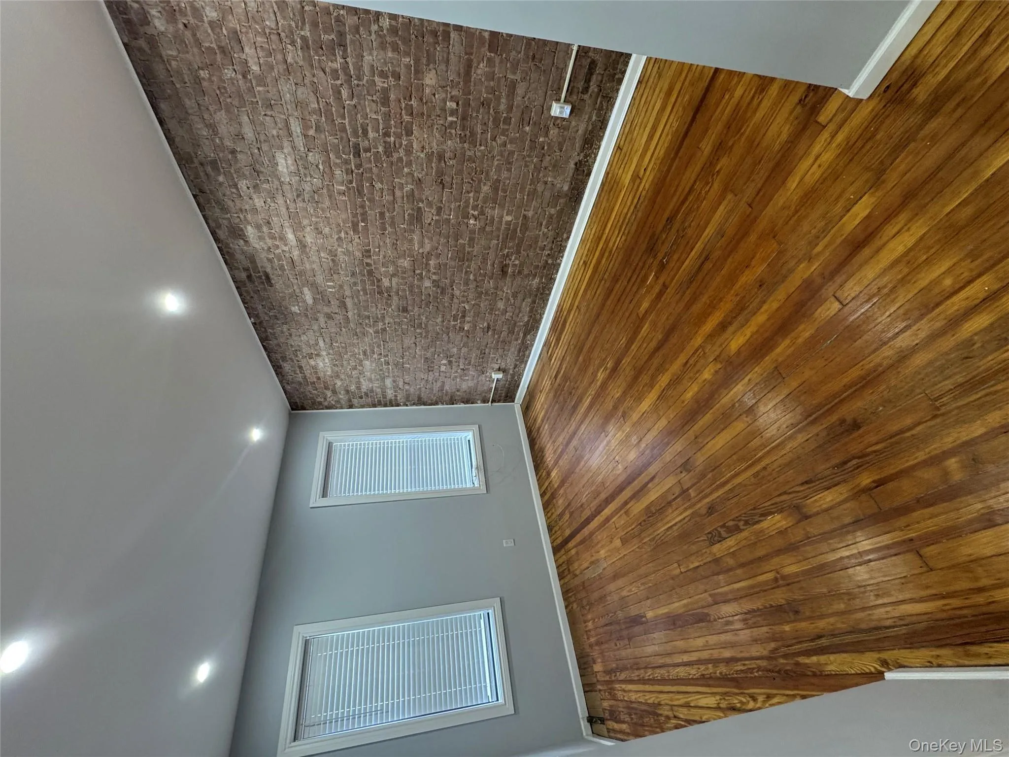 Spare room with dark wood-style floors, brick wall, and recessed lighting Spare room with dark wood-style floors, brick wall, and recessed lighting