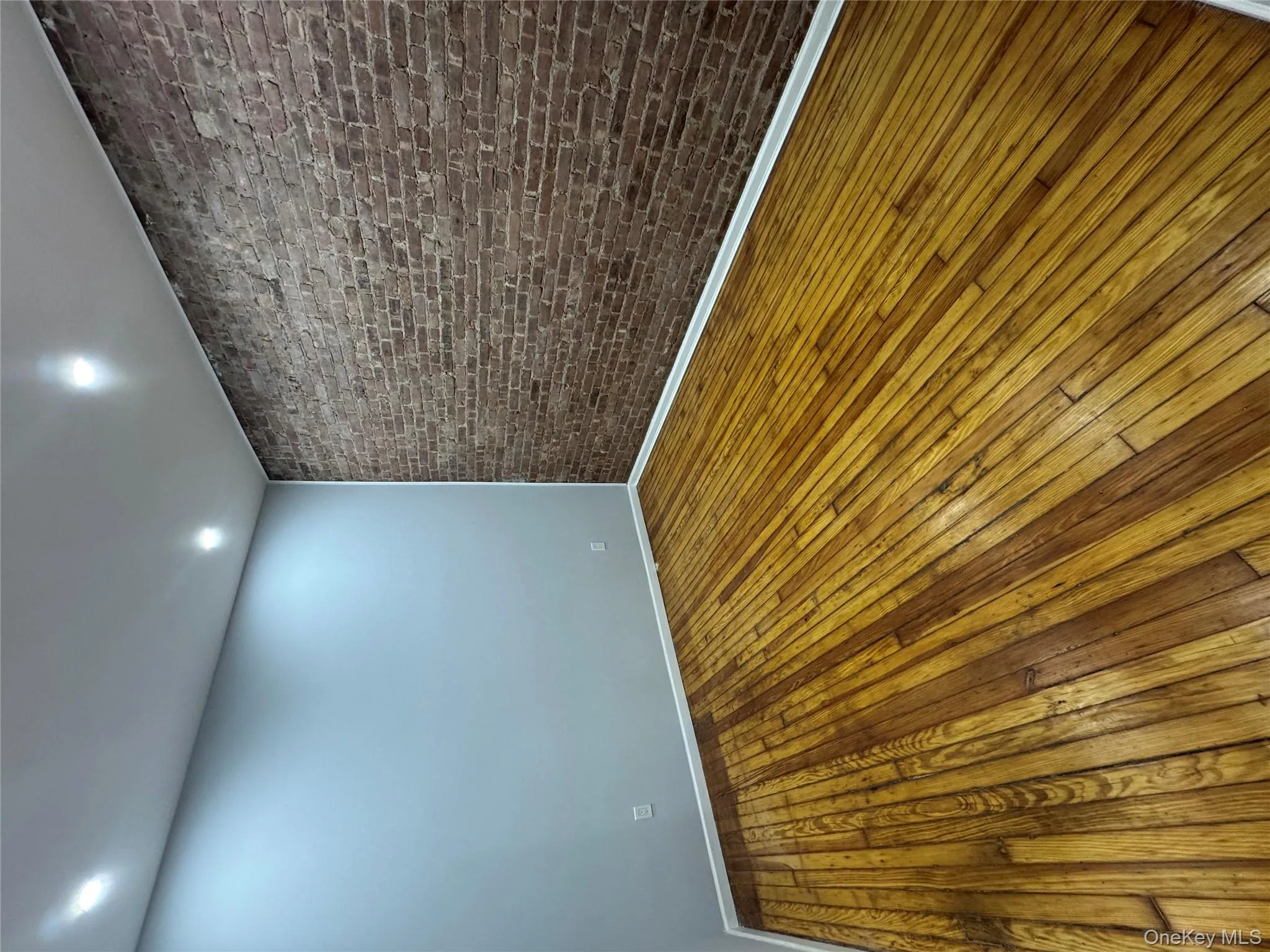 Unfurnished room with brick wall, hardwood / wood-style floors, and recessed lighting Unfurnished room with brick wall, hardwood / wood-style floors, and recessed lighting