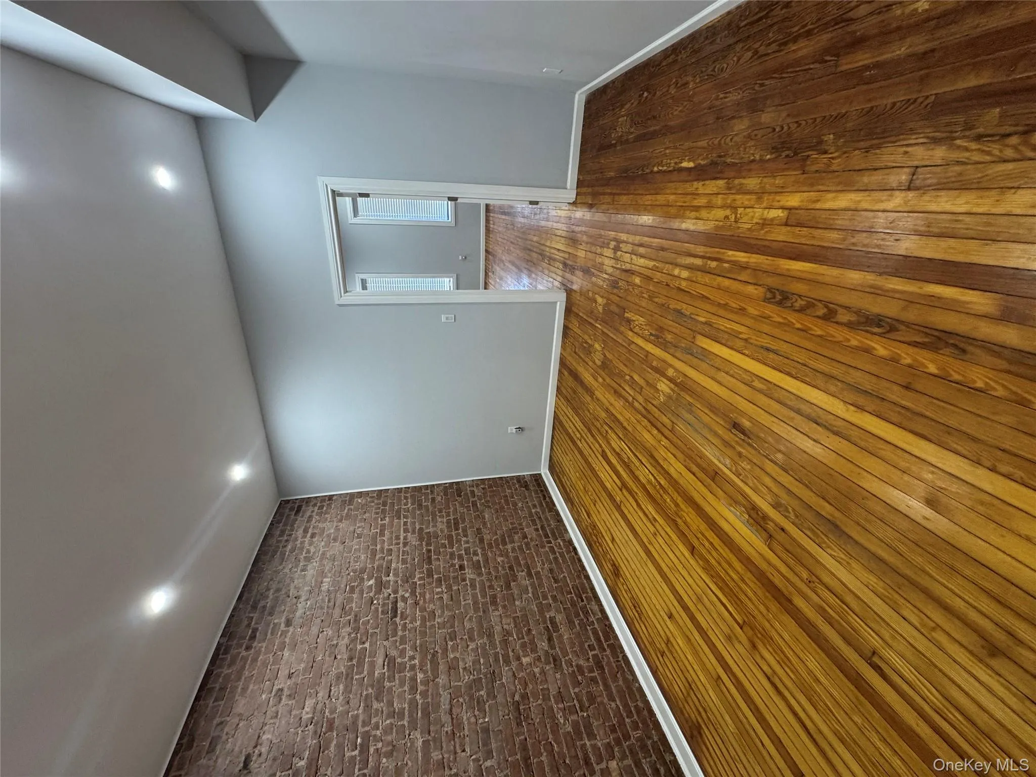 Unfurnished room with brick wall, dark wood-style floors, and recessed lighting Unfurnished room with brick wall, dark wood-style floors, and recessed lighting