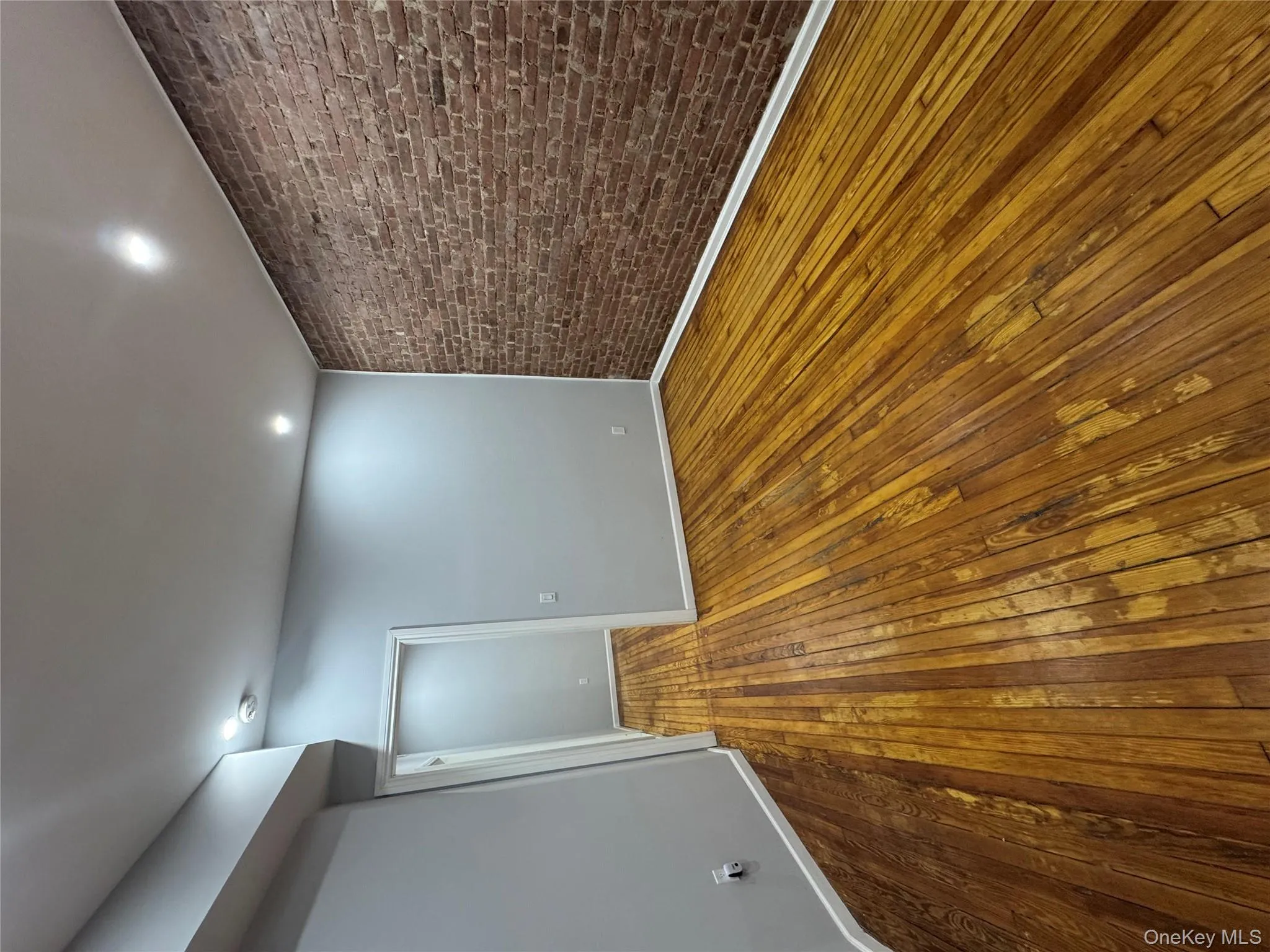 Unfurnished room featuring brick wall, dark wood-style floors, and recessed lighting Unfurnished room featuring brick wall, dark wood-style floors, and recessed lighting