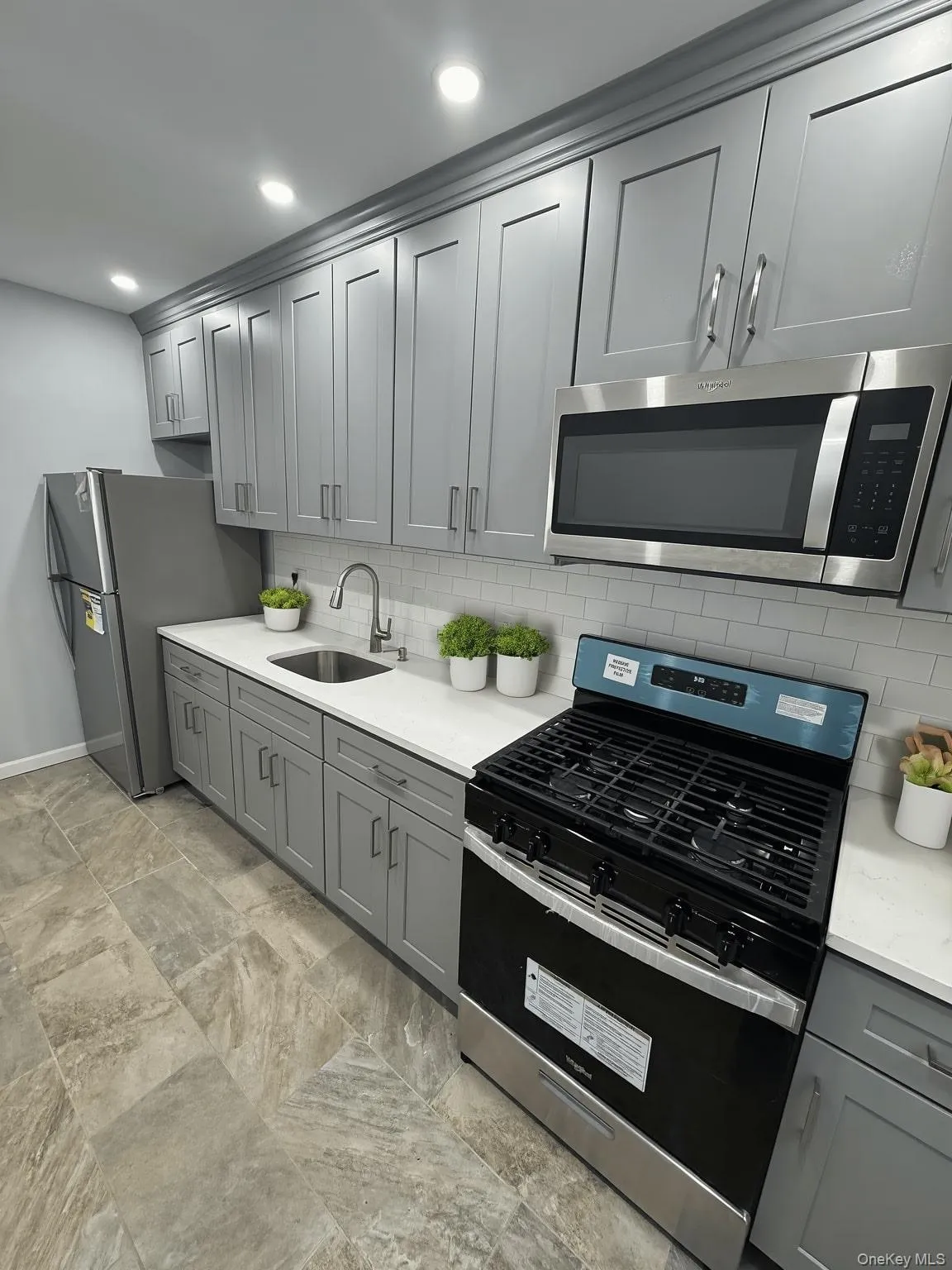 Kitchen featuring stainless steel appliances, gray cabinets, light stone counters, backsplash, and recessed lighting Kitchen featuring stainless steel appliances, gray cabinets, light stone counters, backsplash, and recessed lighting