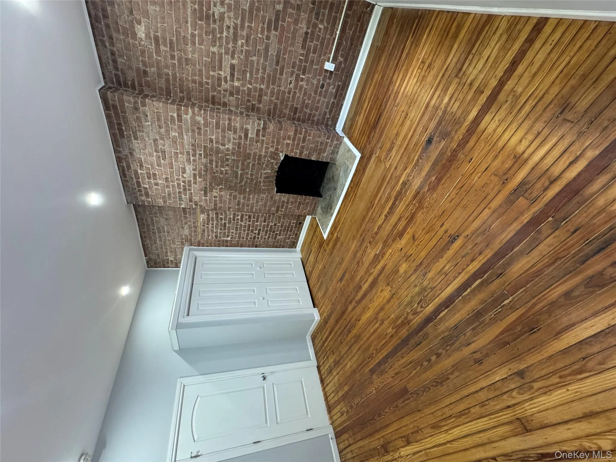 Unfurnished living room with hardwood / wood-style flooring, brick wall, a fireplace, and recessed lighting Unfurnished living room with hardwood / wood-style flooring, brick wall, a fireplace, and recessed lighting