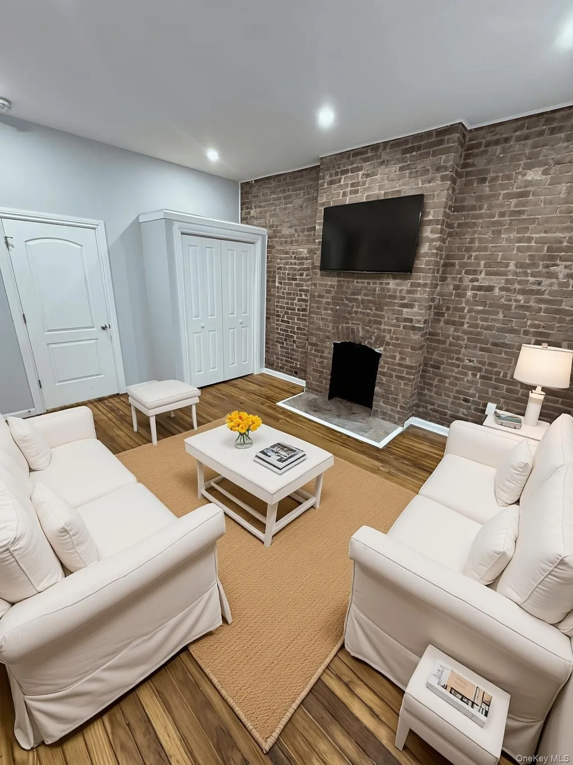 Living room with brick wall, wood finished floors, a fireplace, and recessed lighting Living room with brick wall, wood finished floors, a fireplace, and recessed lighting