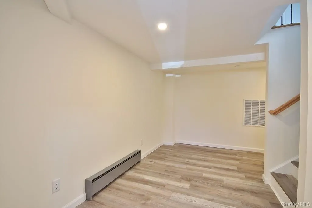 Below grade area featuring a baseboard heating unit, light wood-type flooring, recessed lighting, and stairway Below grade area featuring a baseboard heating unit, light wood-type flooring, recessed lighting, and stairway