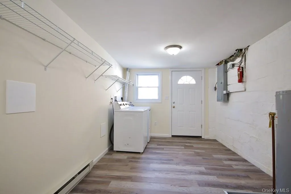 Laundry room with a baseboard heating unit, wood finished floors, water heater, hookup for a washing machine, and electric panel Laundry room with a baseboard heating unit, wood finished floors, water heater, hookup for a washing machine, and electric panel