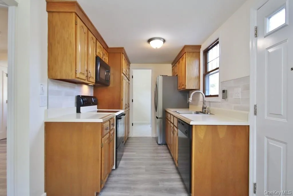 Kitchen with black appliances, tasteful backsplash, brown cabinets, and light countertops Kitchen with black appliances, tasteful backsplash, brown cabinets, and light countertops