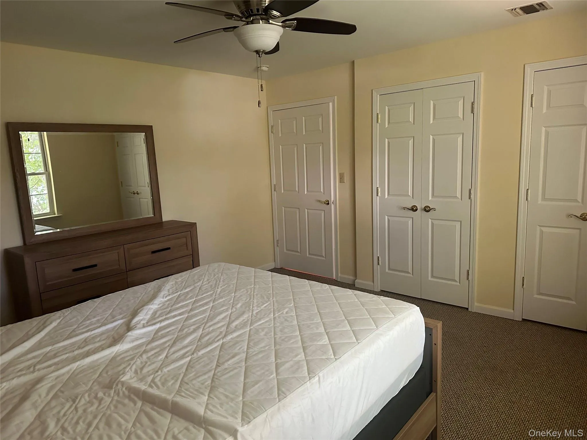 Bedroom featuring dark colored carpet, two closets, and a ceiling fan Bedroom featuring dark colored carpet, two closets, and a ceiling fan