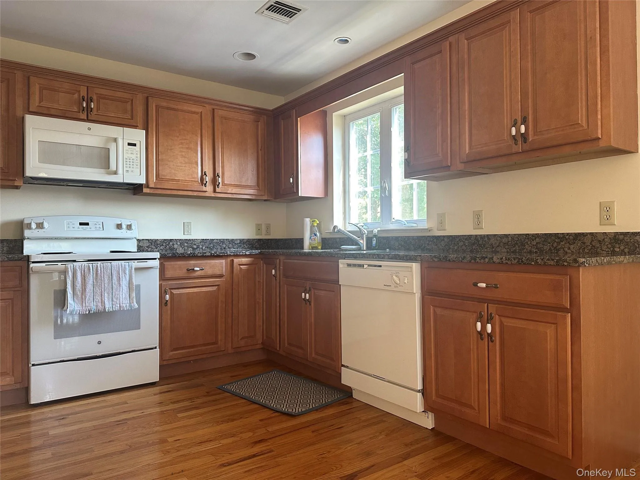 Kitchen featuring white appliances, brown cabinets, dark wood-style flooring, and dark stone counters Kitchen featuring white appliances, brown cabinets, dark wood-style flooring, and dark stone counters