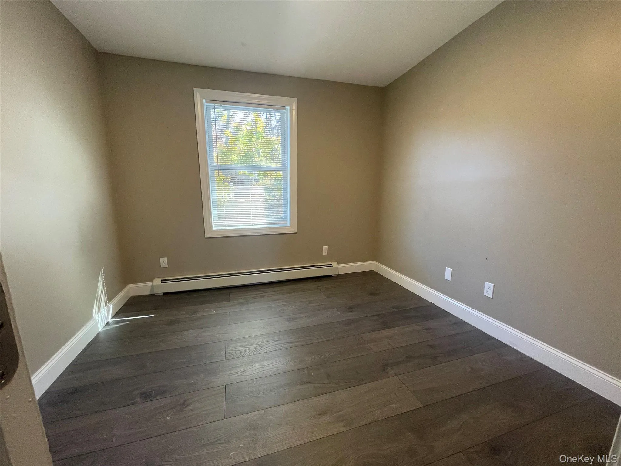 Empty room featuring a baseboard heating unit and dark wood-style flooring Empty room featuring a baseboard heating unit and dark wood-style flooring