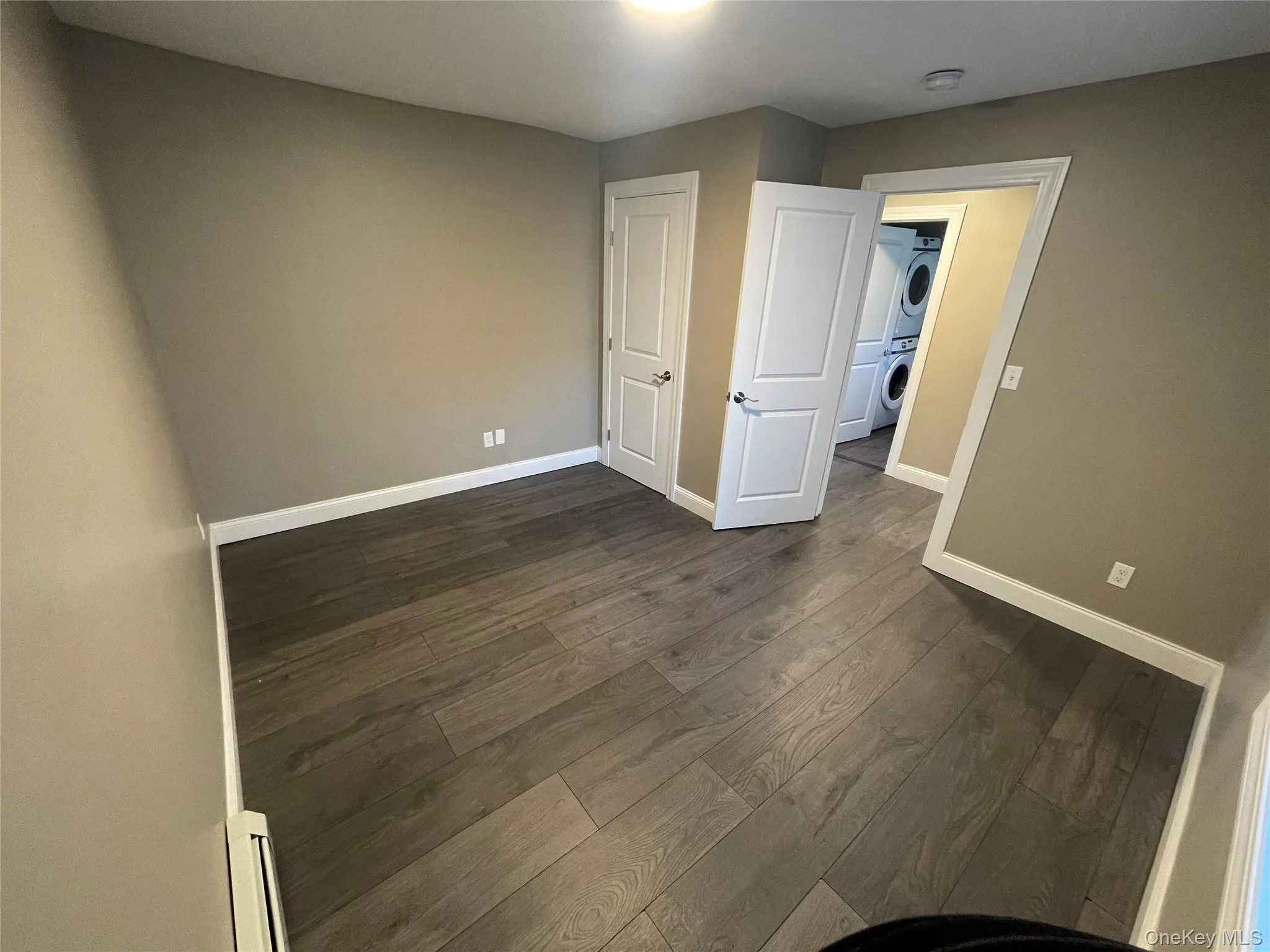 Unfurnished bedroom with stacked washer / drying machine and dark wood-style flooring Unfurnished bedroom with stacked washer / drying machine and dark wood-style flooring