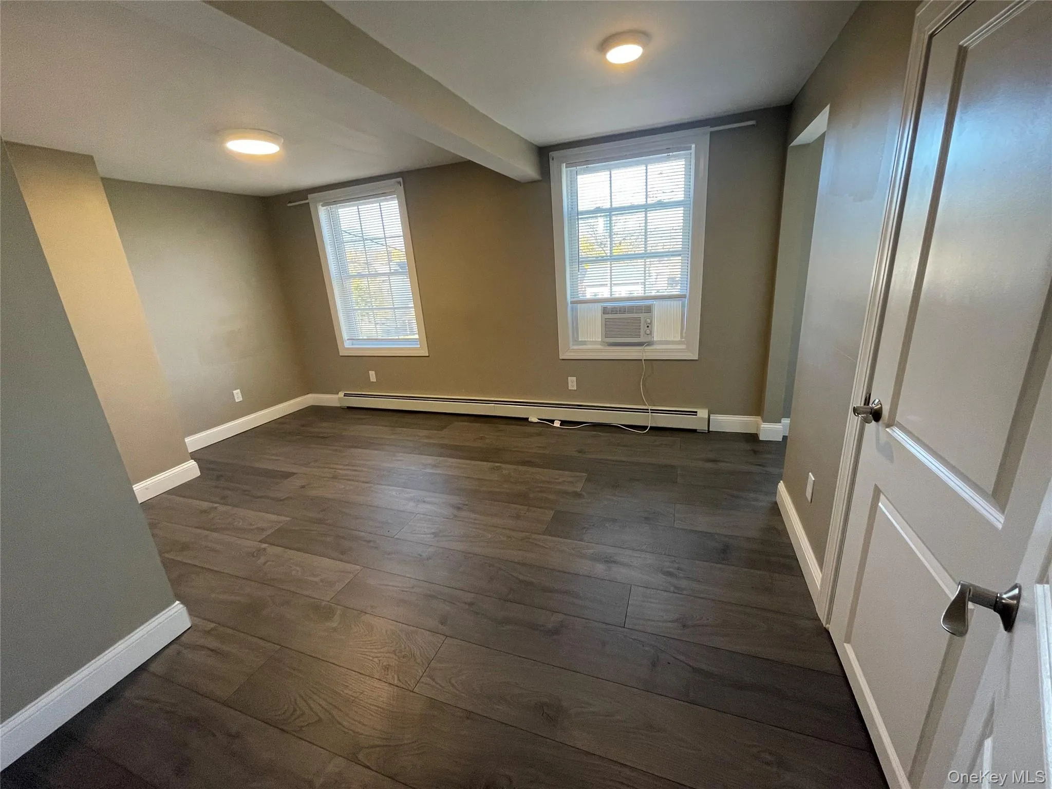 Spare room featuring dark wood-style floors, beam ceiling, a baseboard radiator, and cooling unit Spare room featuring dark wood-style floors, beam ceiling, a baseboard radiator, and cooling unit