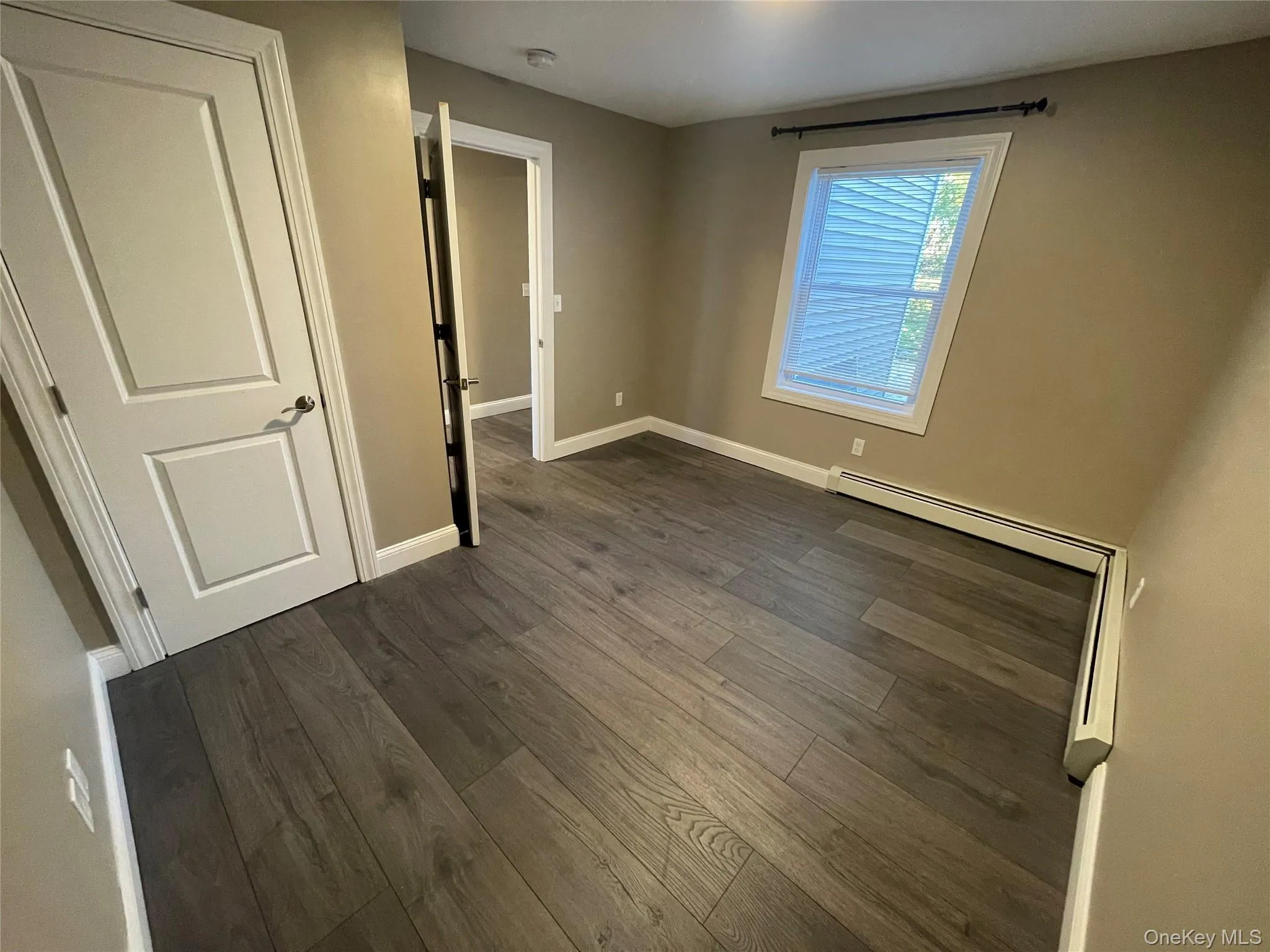 Unfurnished bedroom featuring dark wood-style flooring and a baseboard heating unit Unfurnished bedroom featuring dark wood-style flooring and a baseboard heating unit