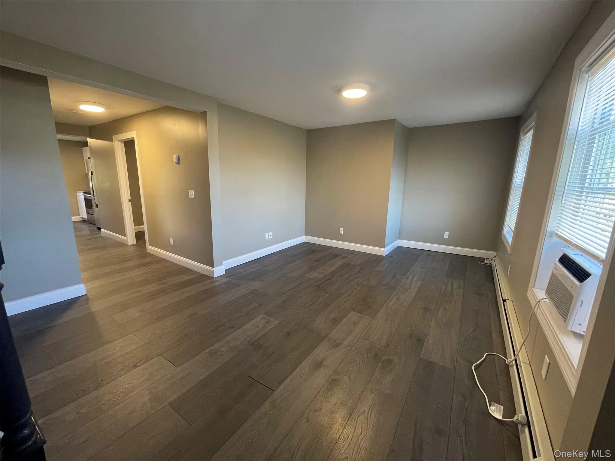 Empty room with a baseboard radiator, dark wood-type flooring, and cooling unit Empty room with a baseboard radiator, dark wood-type flooring, and cooling unit