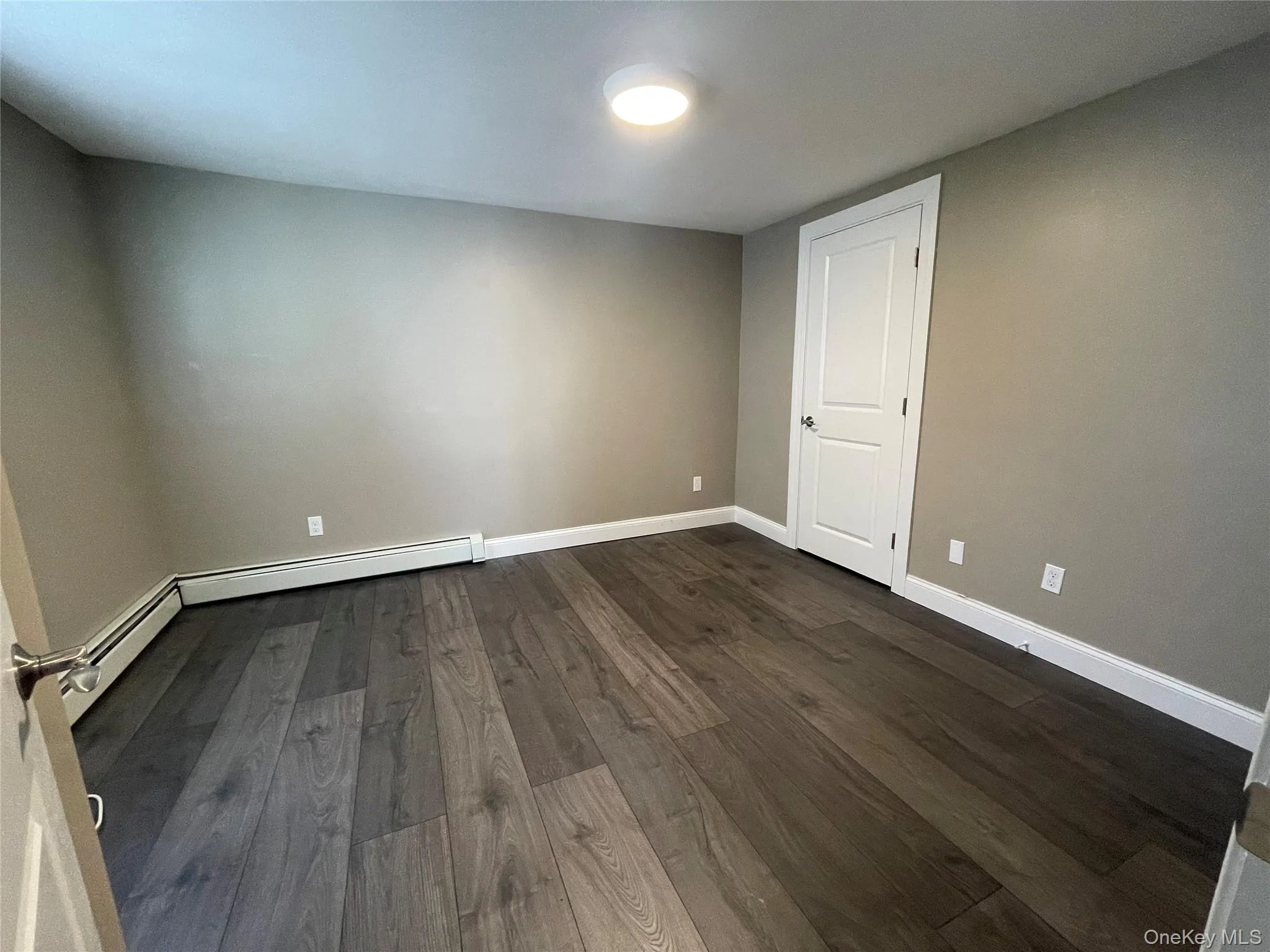 Empty room featuring dark wood finished floors and a baseboard heating unit Empty room featuring dark wood finished floors and a baseboard heating unit