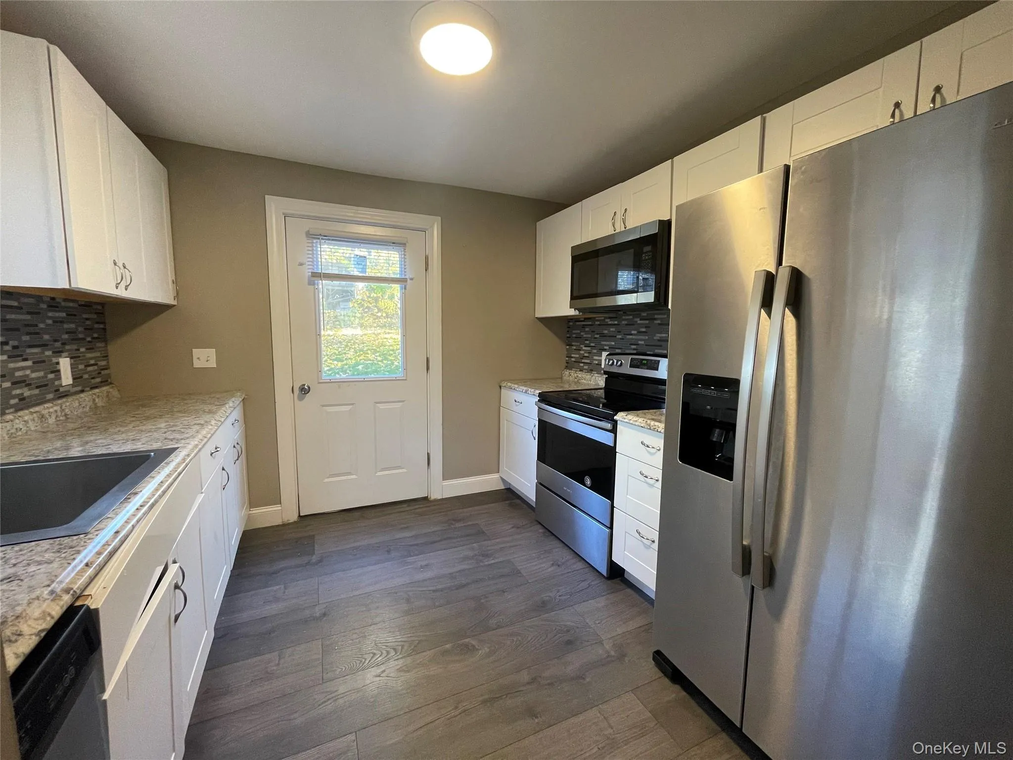 Kitchen featuring appliances with stainless steel finishes, tasteful backsplash, white cabinets, dark wood-type flooring, and light stone counters Kitchen featuring appliances with stainless steel finishes, tasteful backsplash, white cabinets, dark wood-type flooring, and light stone counters