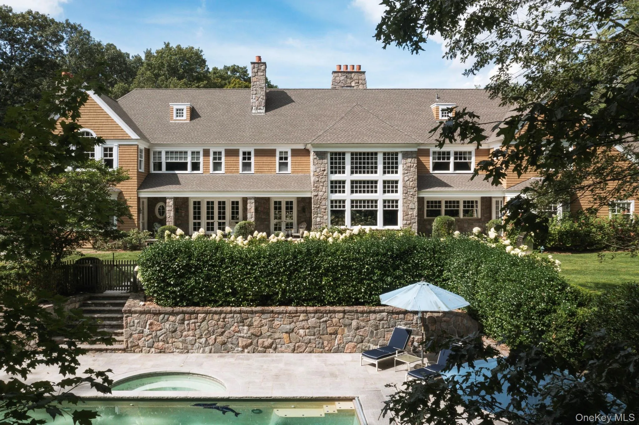 Rear view of house with a patio, stone siding, a chimney, and an in-ground hot tub Rear view of house with a patio, stone siding, a chimney, and an in-ground hot tub