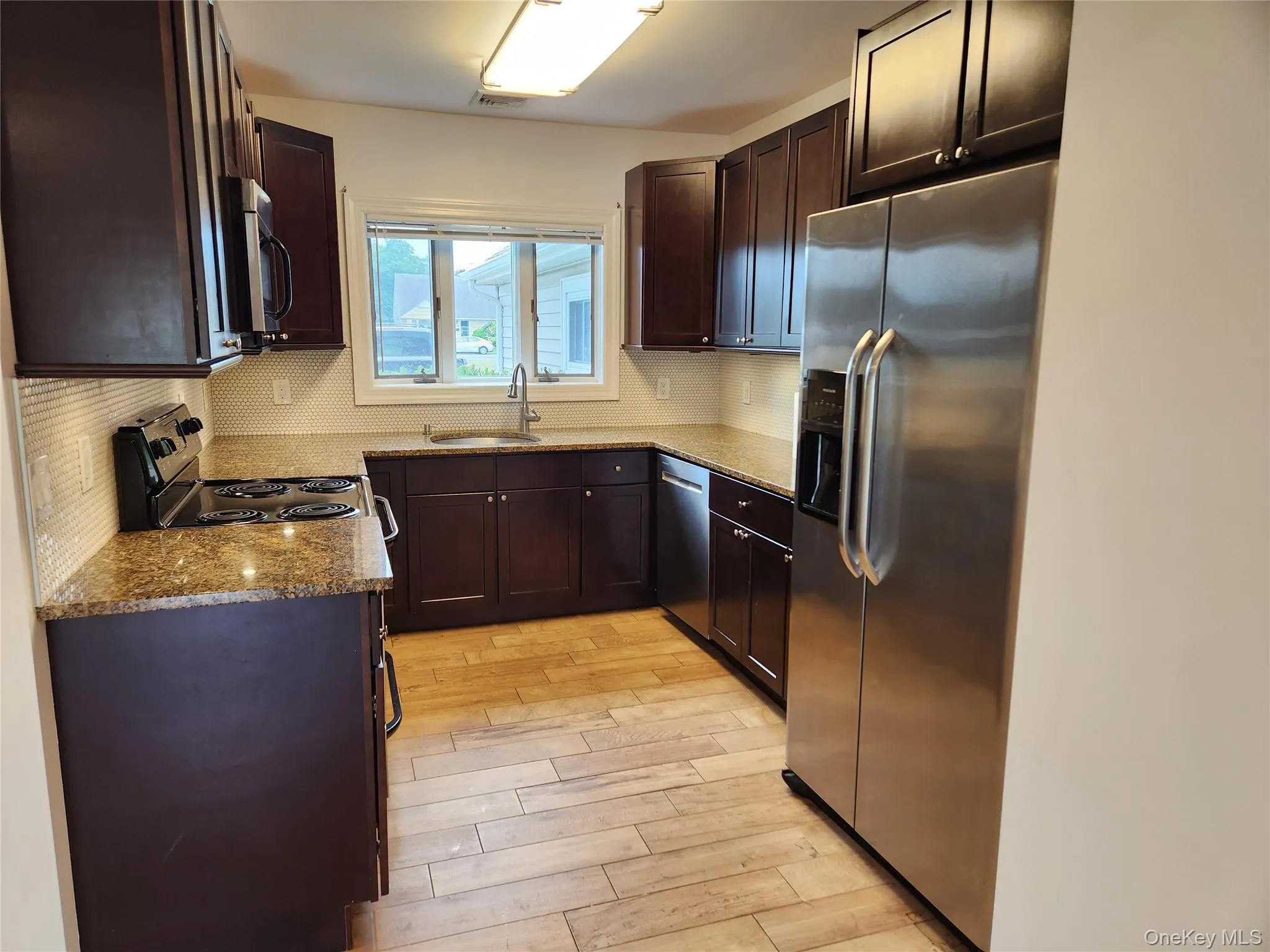 Kitchen featuring light stone countertops, stainless steel appliances, light wood-style flooring, and dark brown cabinets Kitchen featuring light stone countertops, stainless steel appliances, light wood-style flooring, and dark brown cabinets