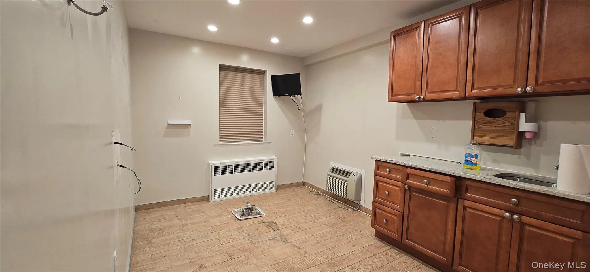Kitchen featuring light stone counters, recessed lighting, light wood-style flooring, radiator, and brown cabinetry Kitchen featuring light stone counters, recessed lighting, light wood-style flooring, radiator, and brown cabinetry