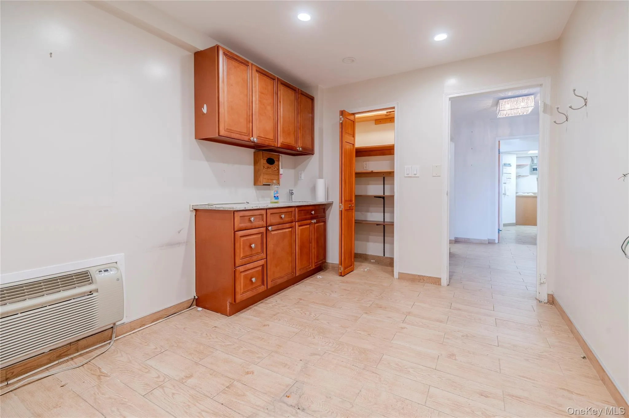 Kitchen with light countertops, brown cabinets, a wall unit AC, and recessed lighting Kitchen with light countertops, brown cabinets, a wall unit AC, and recessed lighting