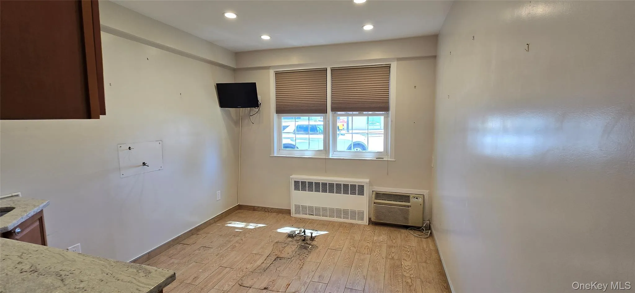 Kitchen with light wood-type flooring, radiator, light stone counters, recessed lighting, and a wall mounted air conditioner Kitchen with light wood-type flooring, radiator, light stone counters, recessed lighting, and a wall mounted air conditioner