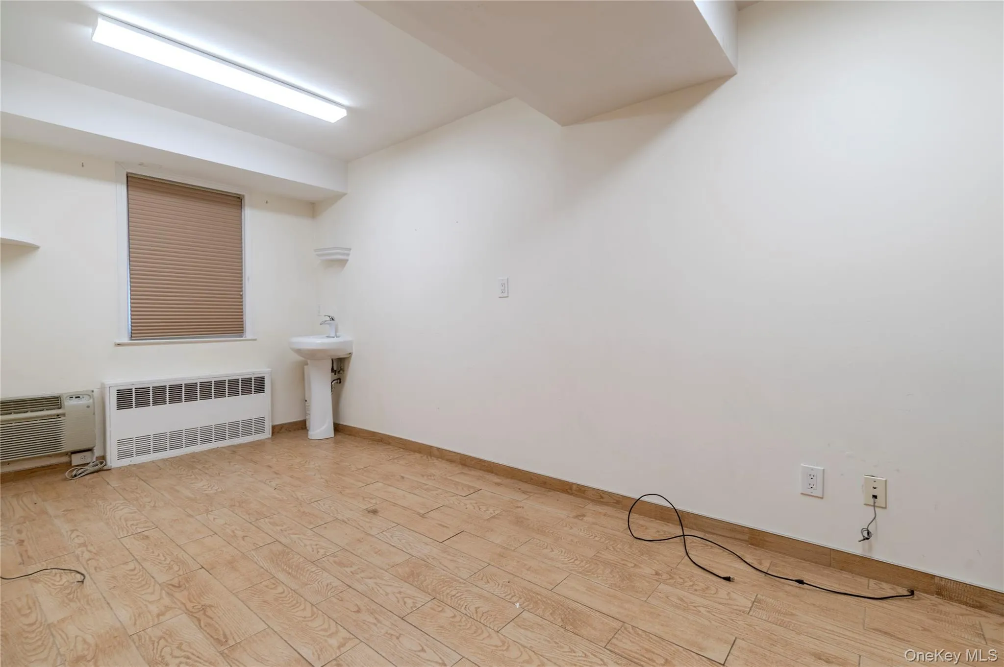 Empty room featuring radiator heating unit, light wood-style floors, and a wall mounted air conditioner Empty room featuring radiator heating unit, light wood-style floors, and a wall mounted air conditioner