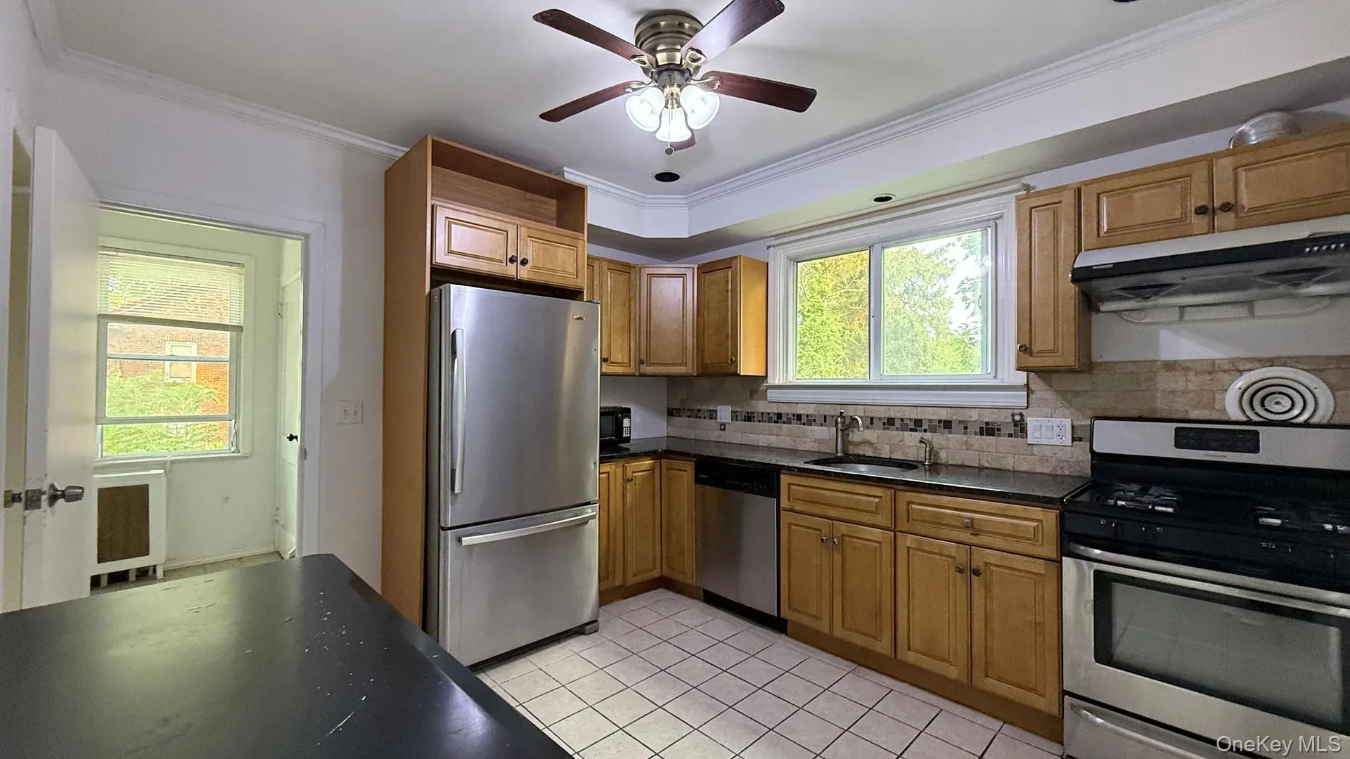 Kitchen featuring stainless steel appliances, crown molding, extractor fan, light tile patterned floors, and decorative backsplash Kitchen featuring stainless steel appliances, crown molding, extractor fan, light tile patterned floors, and decorative backsplash