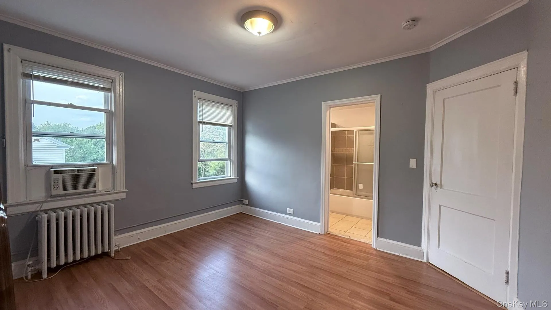 Unfurnished bedroom featuring radiator heating unit, wood finished floors, ornamental molding, and connected bathroom Unfurnished bedroom featuring radiator heating unit, wood finished floors, ornamental molding, and connected bathroom