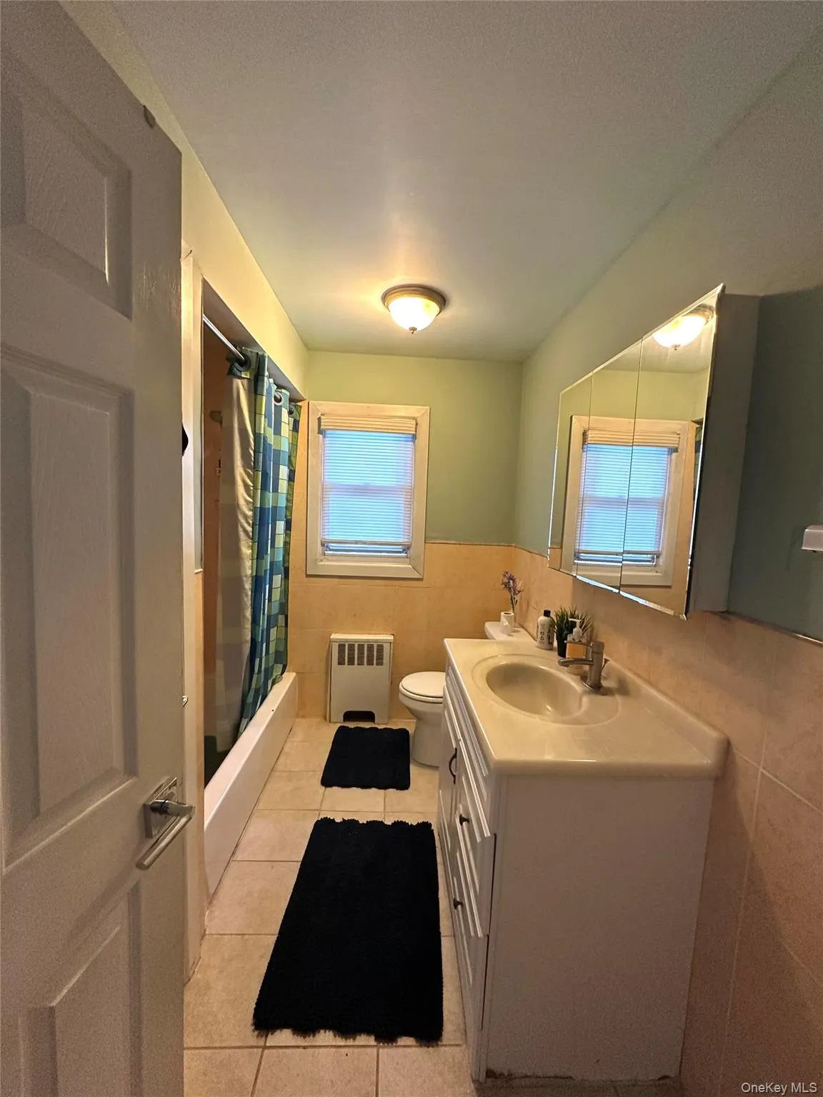 Bathroom featuring tile walls, vanity, light tile patterned floors, wainscoting, and shower / bathtub combination with curtain Bathroom featuring tile walls, vanity, light tile patterned floors, wainscoting, and shower / bathtub combination with curtain