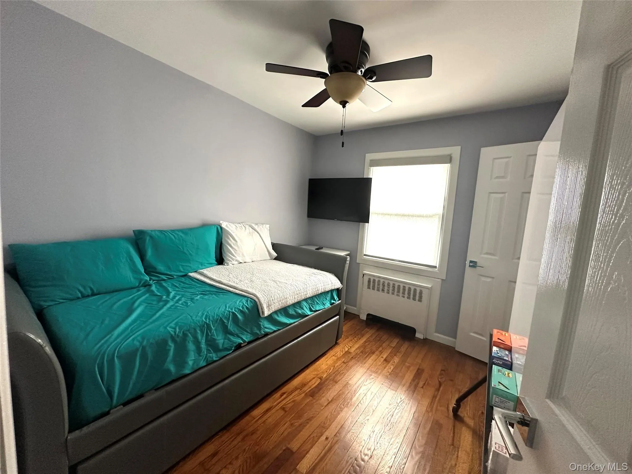 Bedroom featuring wood-type flooring, radiator heating unit, and ceiling fan Bedroom featuring wood-type flooring, radiator heating unit, and ceiling fan