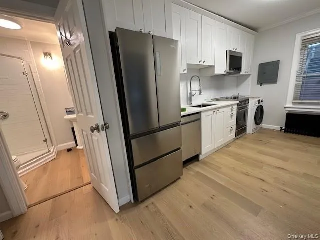 Kitchen featuring white cabinets, appliances with stainless steel finishes, light wood-type flooring, ornamental molding, and tasteful backsplash Kitchen featuring white cabinets, appliances with stainless steel finishes, light wood-type flooring, ornamental molding, and tasteful backsplash