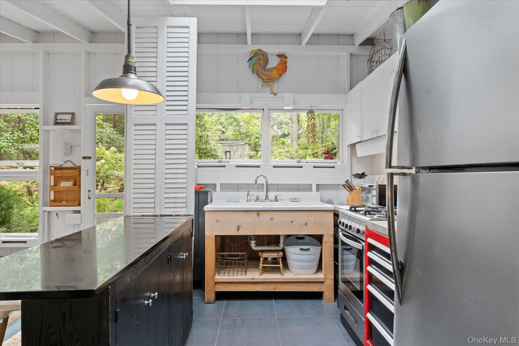 Kitchen featuring appliances with stainless steel finishes, dark cabinetry, dark tile patterned floors, dark countertops, and a kitchen island