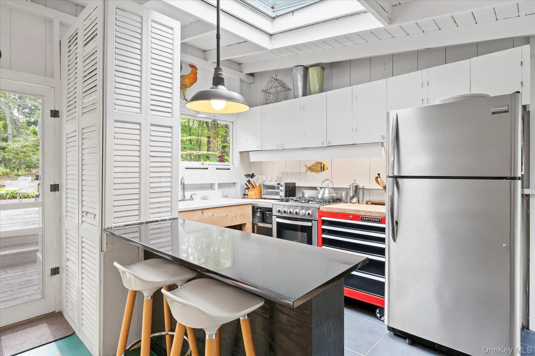 Kitchen featuring stainless steel appliances, a breakfast bar, white cabinetry, decorative light fixtures, and a peninsula