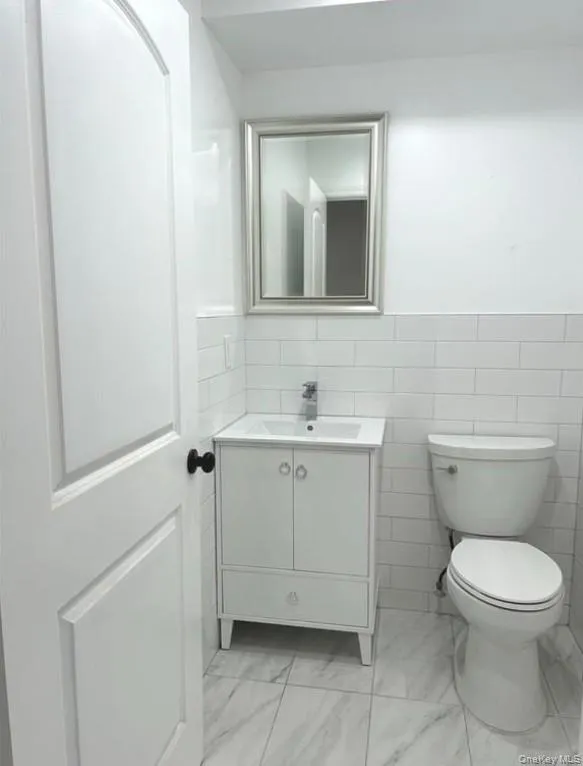 Bathroom featuring tile walls, vanity, a wainscoted wall, and light marble finish floors Bathroom featuring tile walls, vanity, a wainscoted wall, and light marble finish floors
