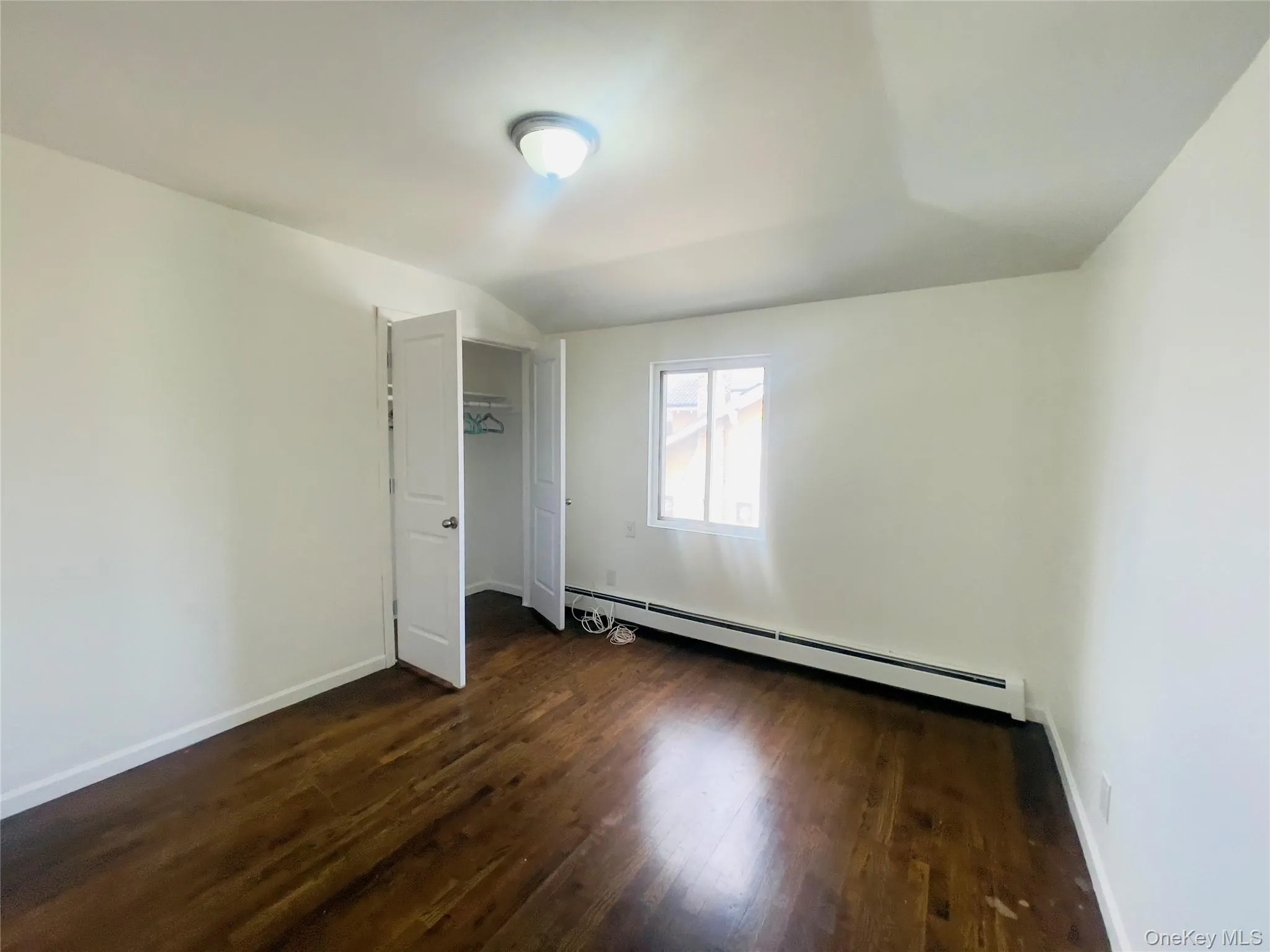 Unfurnished bedroom featuring dark wood finished floors, a baseboard heating unit, and vaulted ceiling Unfurnished bedroom featuring dark wood finished floors, a baseboard heating unit, and vaulted ceiling