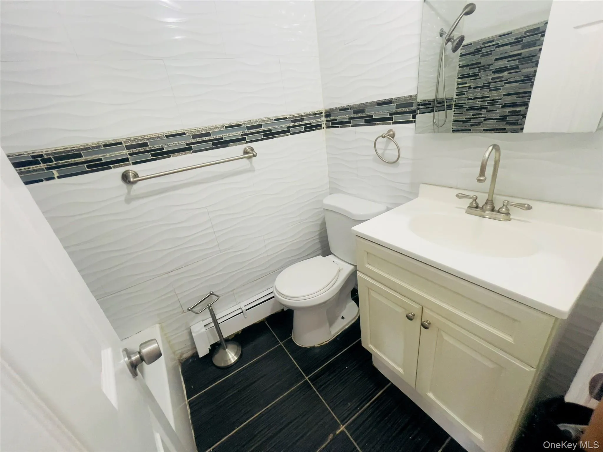 Bathroom featuring tile walls, vanity, a baseboard radiator, dark tile patterned floors, and a tile shower Bathroom featuring tile walls, vanity, a baseboard radiator, dark tile patterned floors, and a tile shower