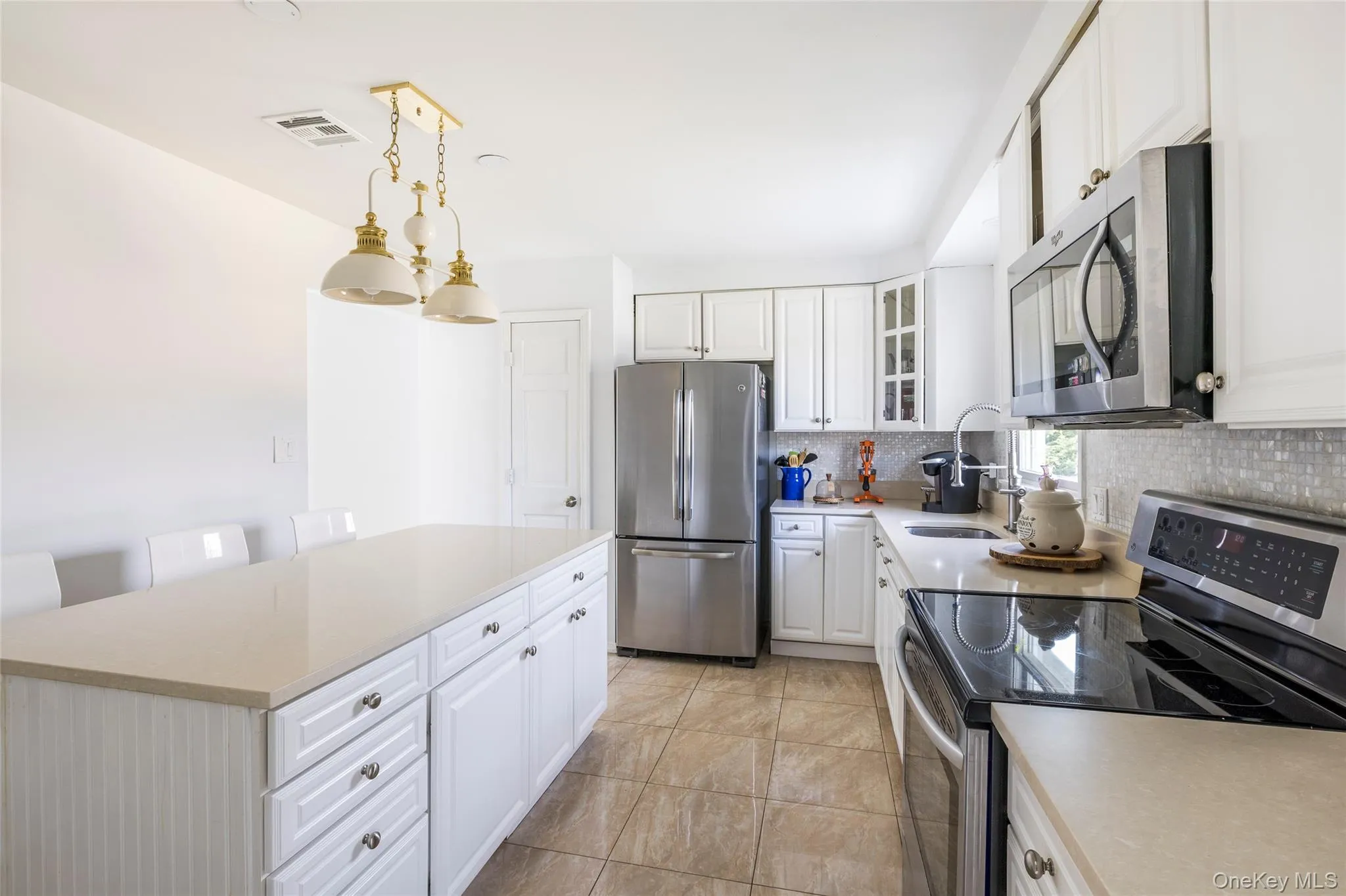 Kitchen featuring appliances with stainless steel finishes, white cabinets, decorative light fixtures, decorative backsplash, and a kitchen island Kitchen featuring appliances with stainless steel finishes, white cabinets, decorative light fixtures, decorative backsplash, and a kitchen island
