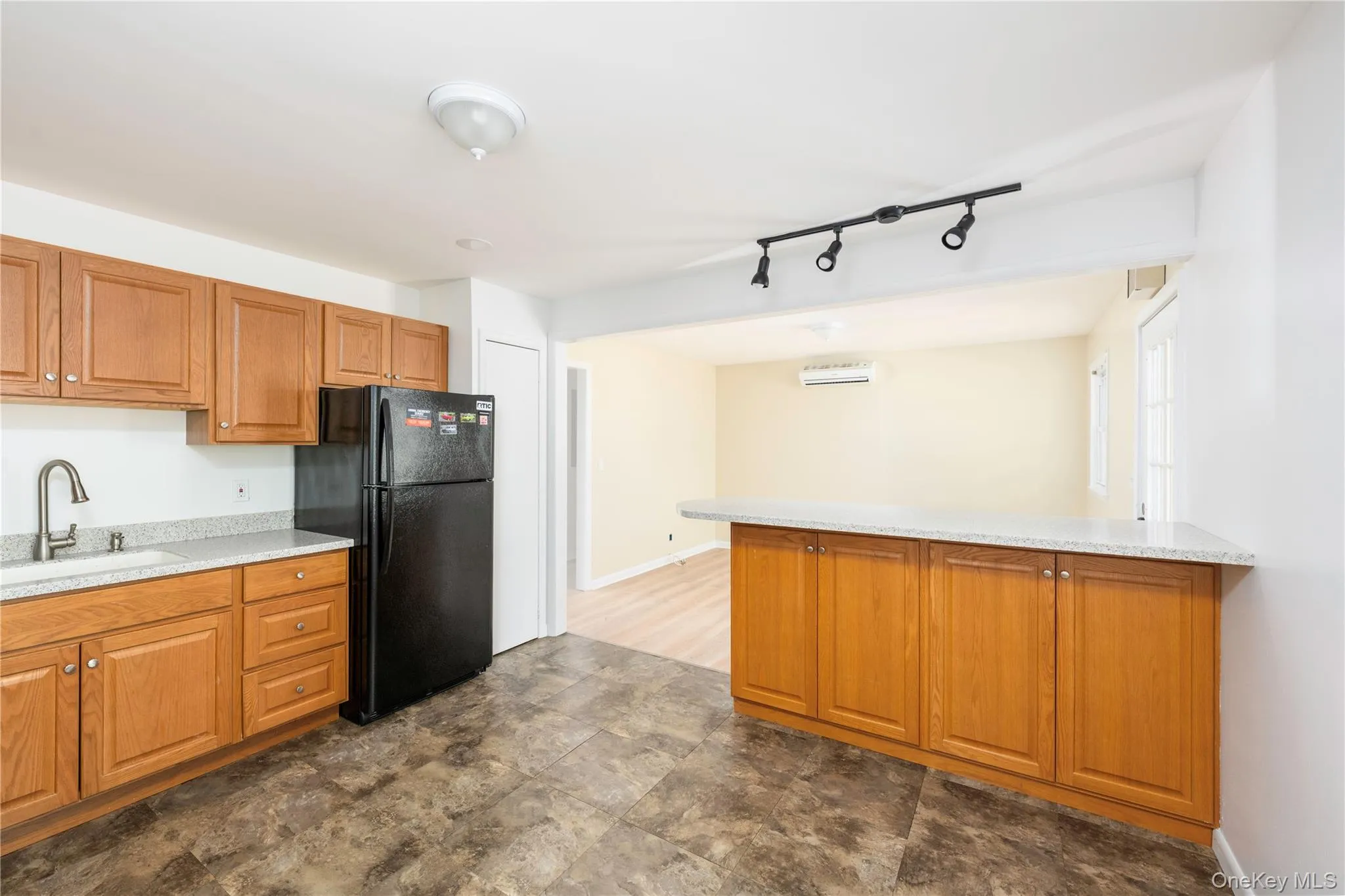Kitchen with freestanding refrigerator, brown cabinets, a peninsula, rail lighting, and light stone counters Kitchen with freestanding refrigerator, brown cabinets, a peninsula, rail lighting, and light stone counters
