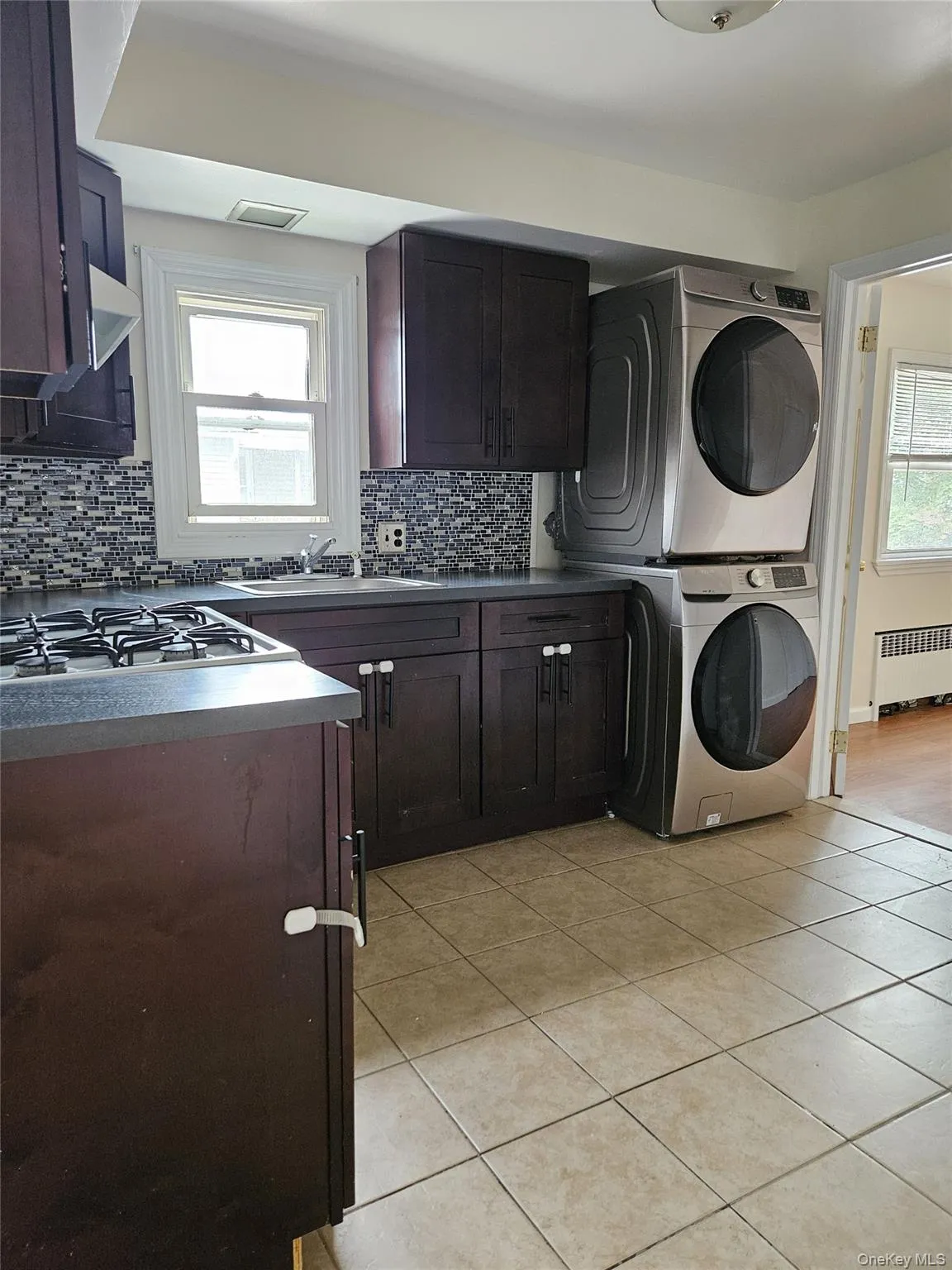 Laundry area featuring radiator heating unit, light tile patterned floors, and estacked washer and dryer Laundry area featuring radiator heating unit, light tile patterned floors, and estacked washer and dryer