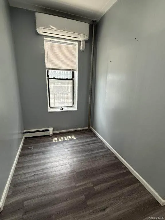 Spare room featuring dark wood-type flooring, a wall mounted AC, and baseboard heating Spare room featuring dark wood-type flooring, a wall mounted AC, and baseboard heating