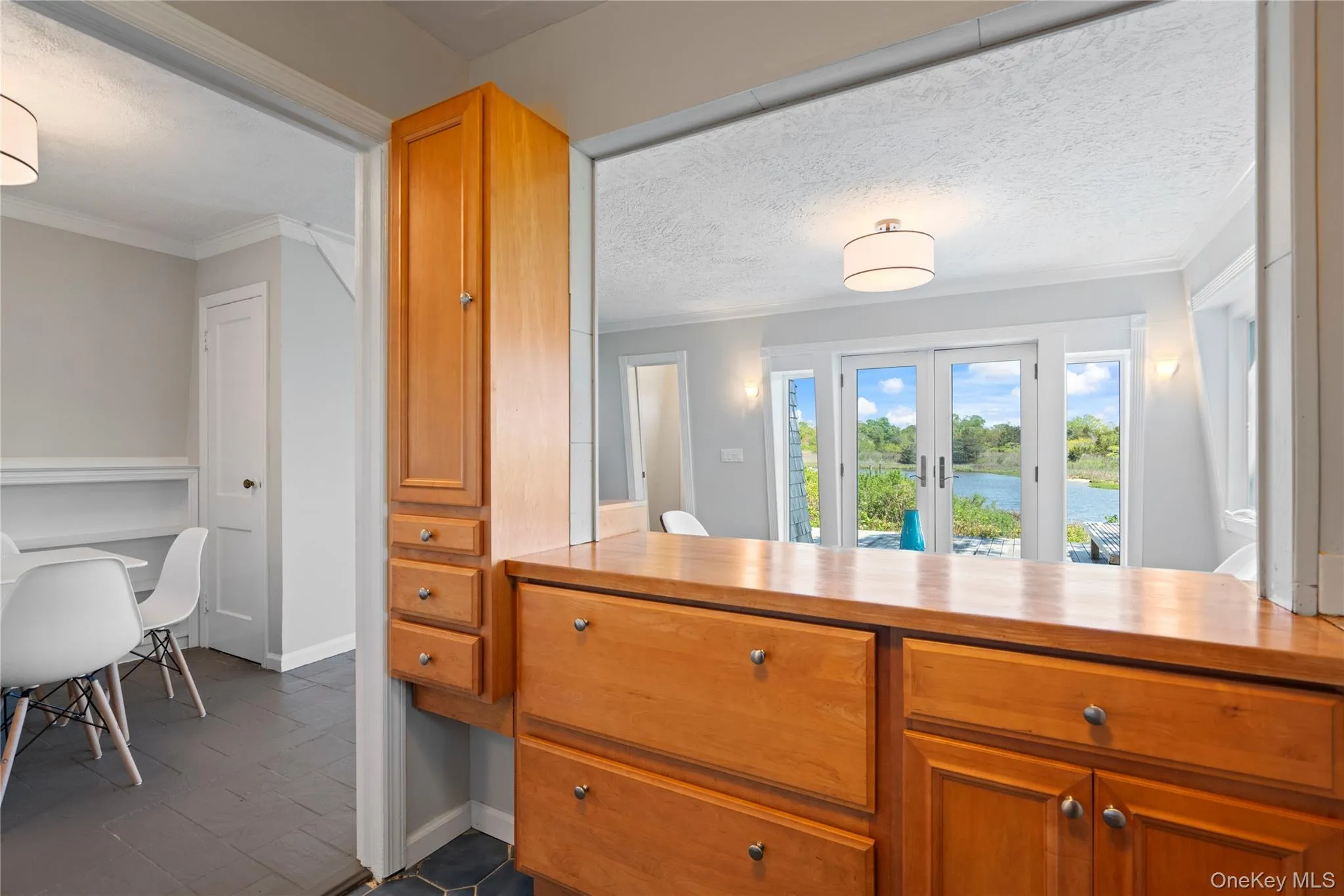 Kitchen featuring a water view, french doors, brown cabinetry, ornamental molding, and a textured ceiling Kitchen featuring a water view, french doors, brown cabinetry, ornamental molding, and a textured ceiling